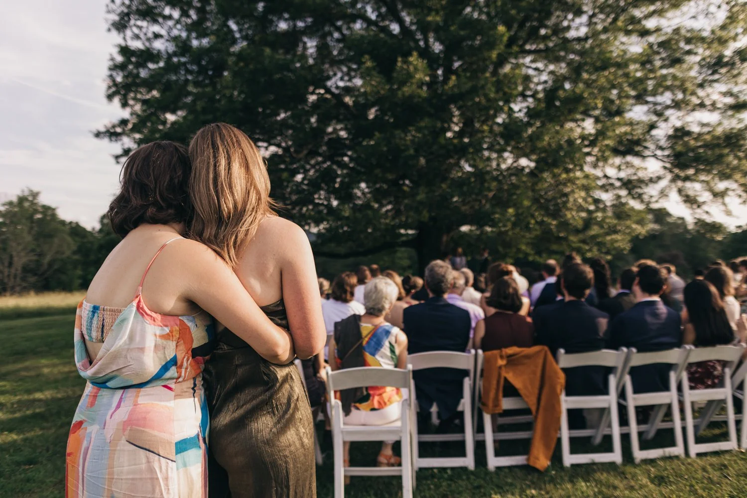 A couple embraces as they watch their friends exchange vows during their wedding at the Red Barn at Hampshire College in Amherst, Massachusetts.