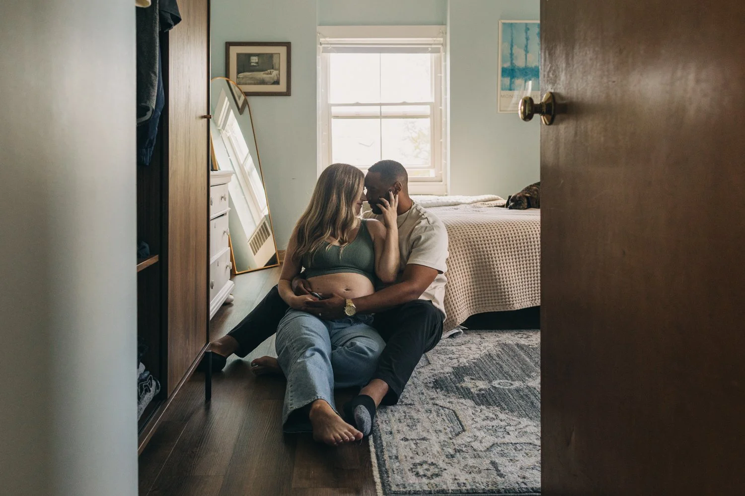 A pregnant woman and her husband sit together on the floor of their apartment during a maternity photo session in western massachusetts.