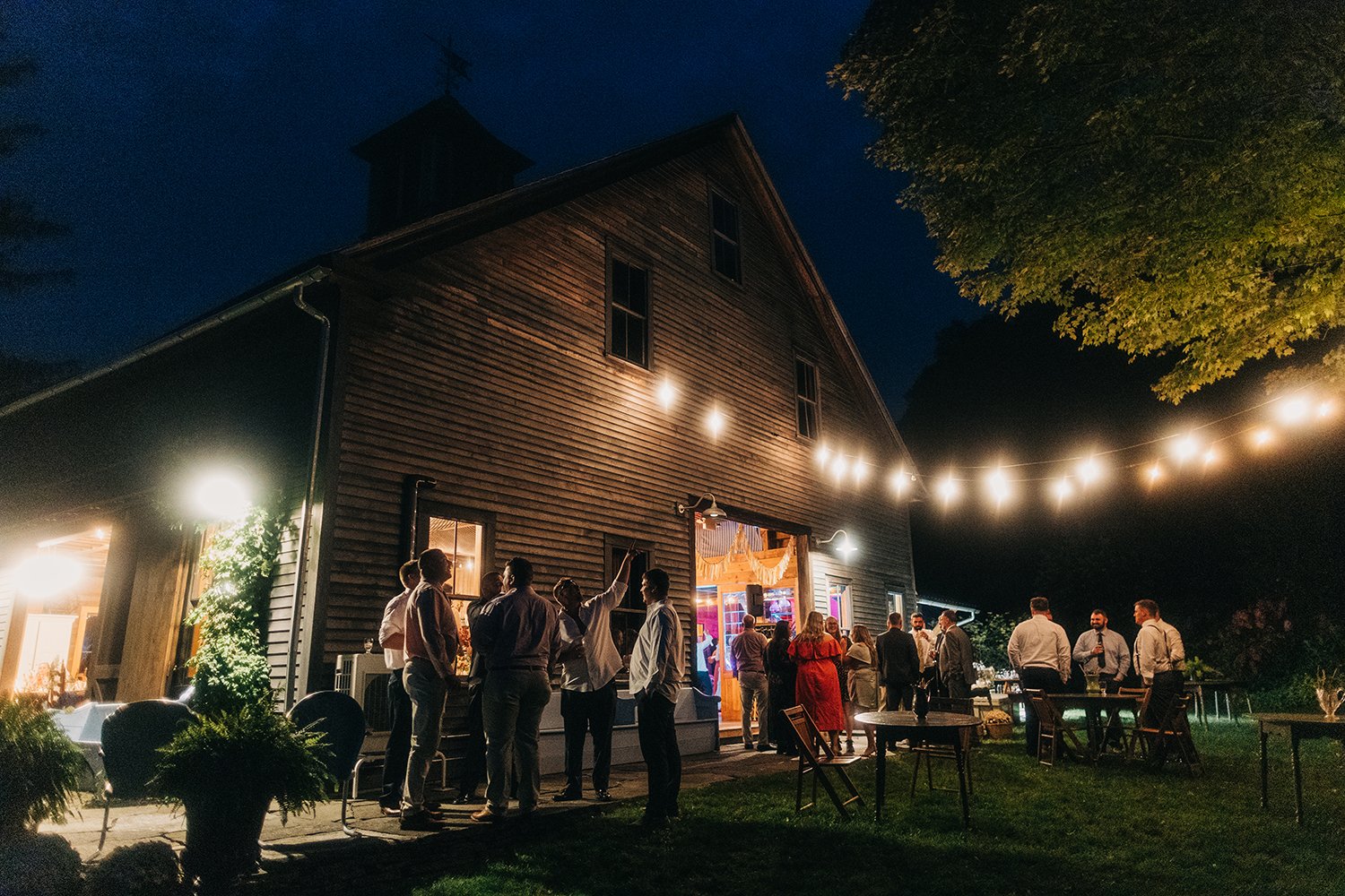 Guests gather under string lights outside of the barn at Gloriosa & co in ashfield massachusetts.