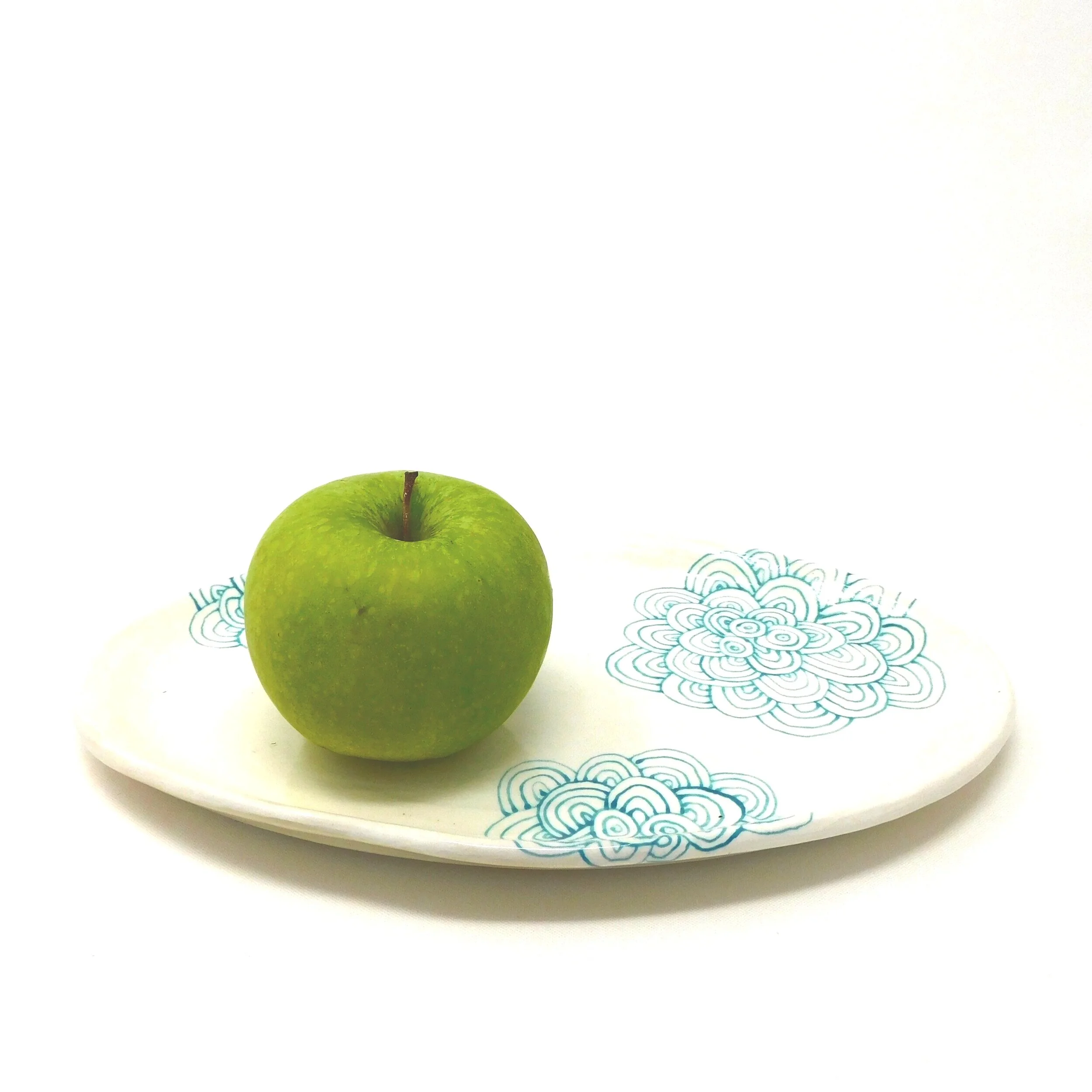 A bright green apple resting on a white plate with blue floral patterns.
