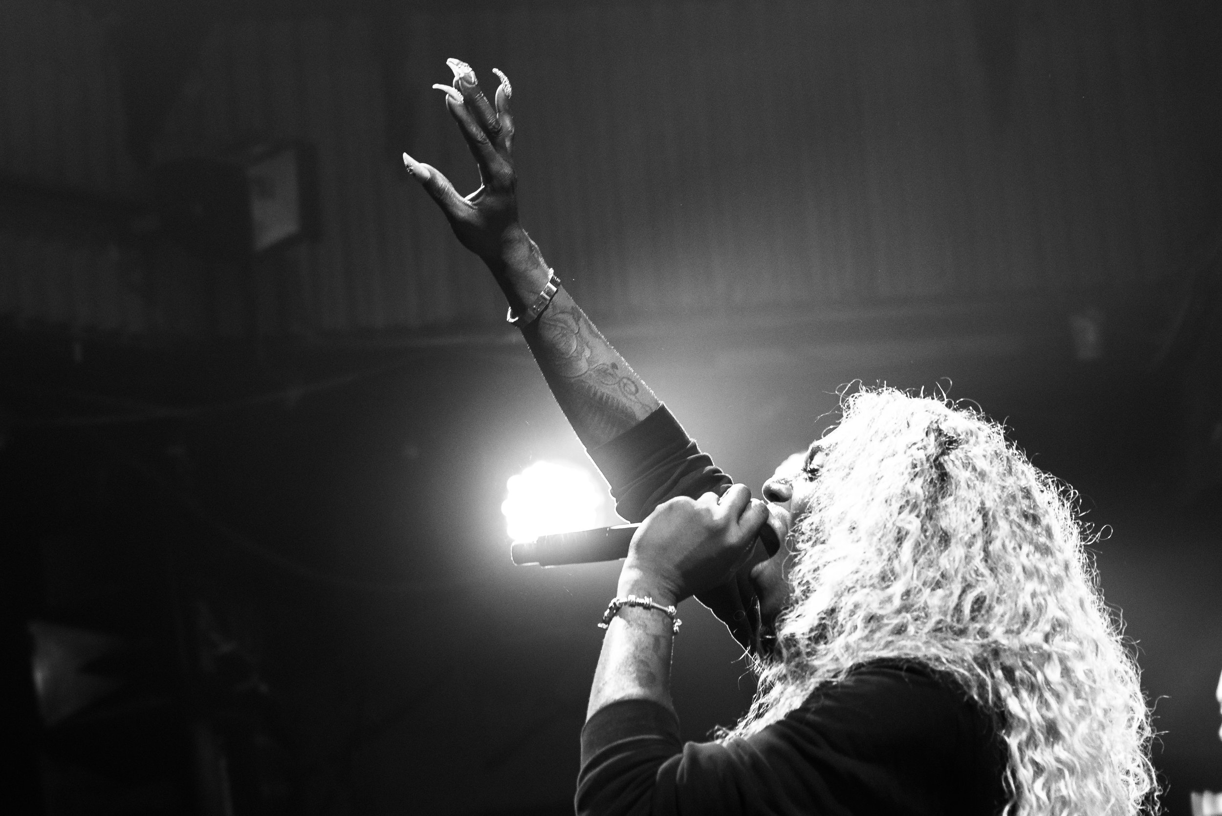 A black and white photo of a woman singing into a microphone on stage with her arm raised.