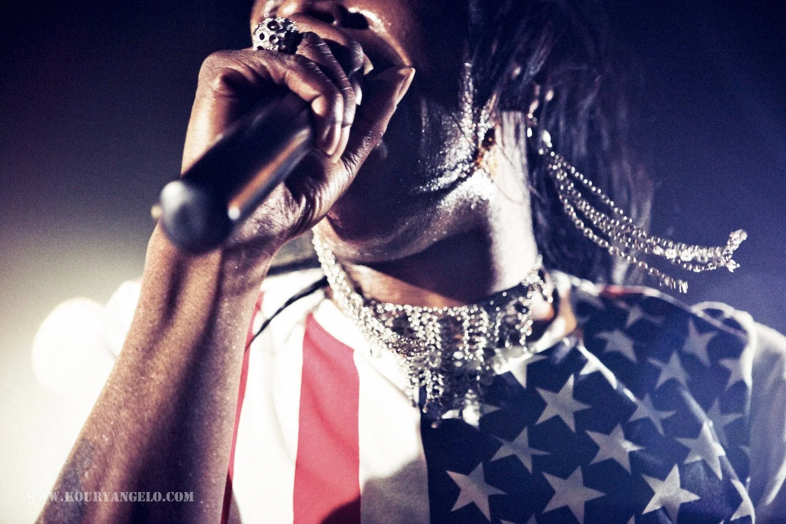 Performer wearing silver jewelry and American flag-themed clothing singing into a microphone.