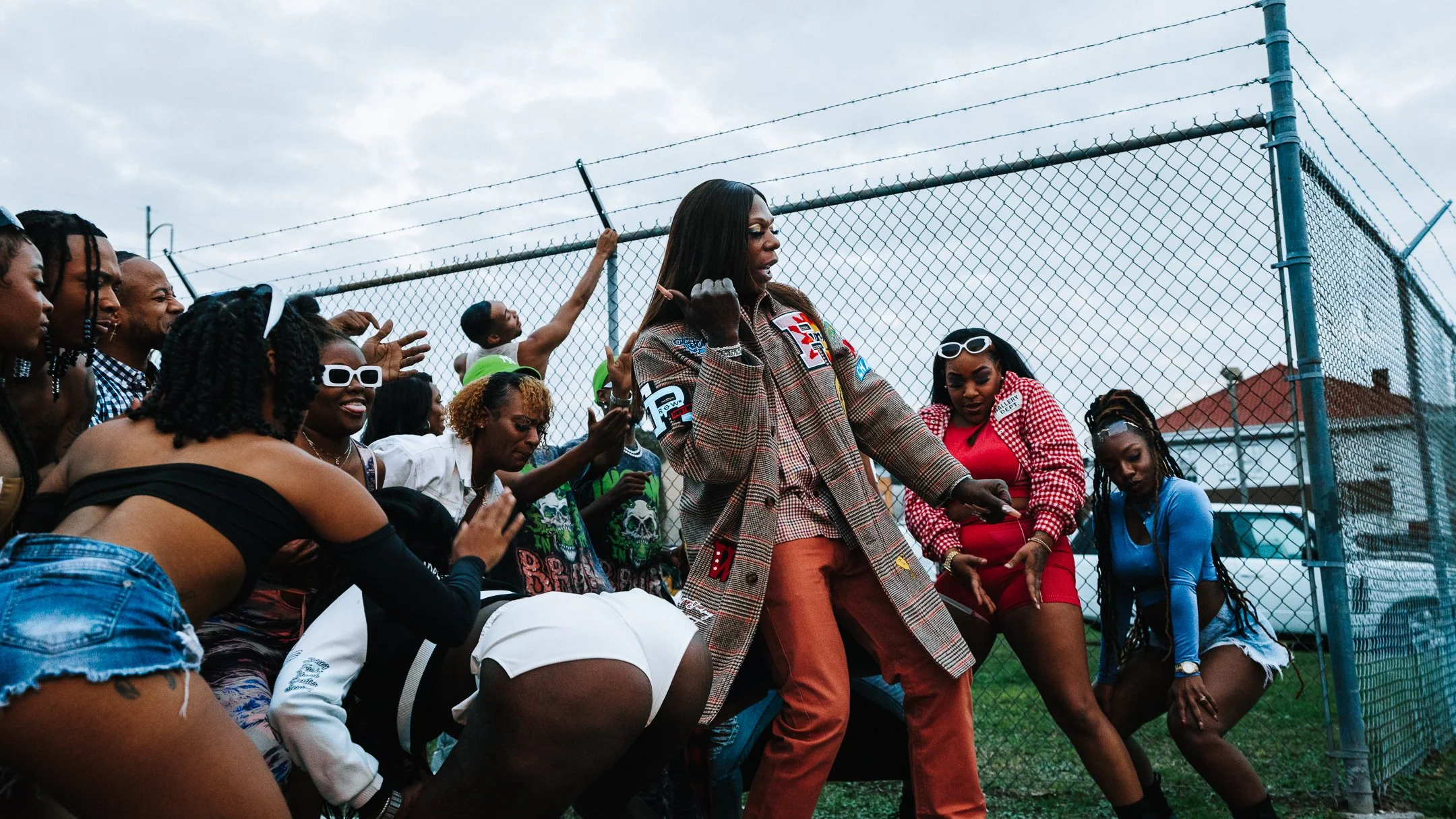 A group of people dancing and enjoying music outdoors near a chain-link fence on a cloudy day.