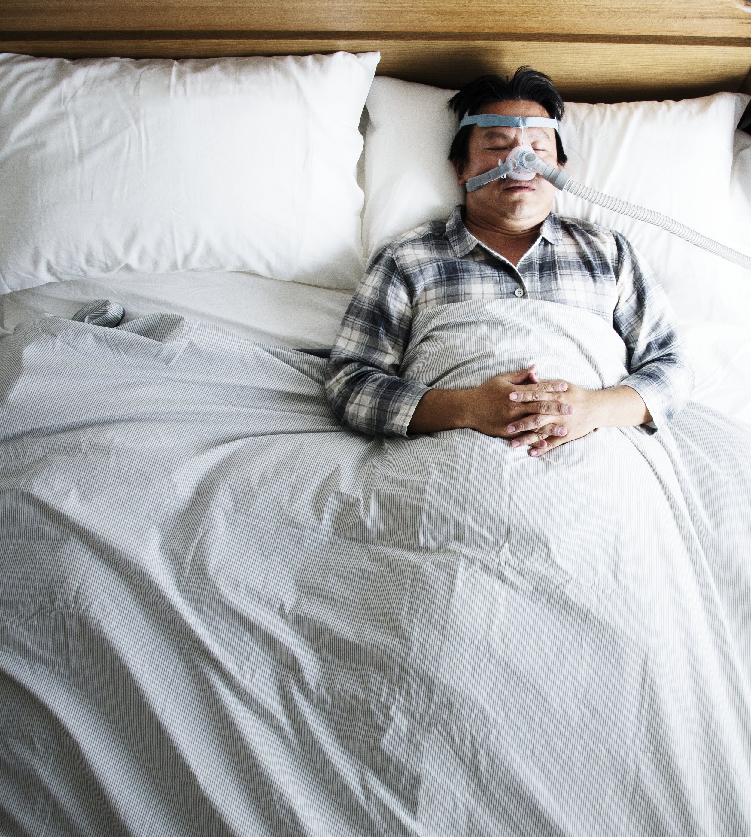 Man sleeping in bed while wearing a CPAP mask, receiving nighttime breathing support for sleep apnea.