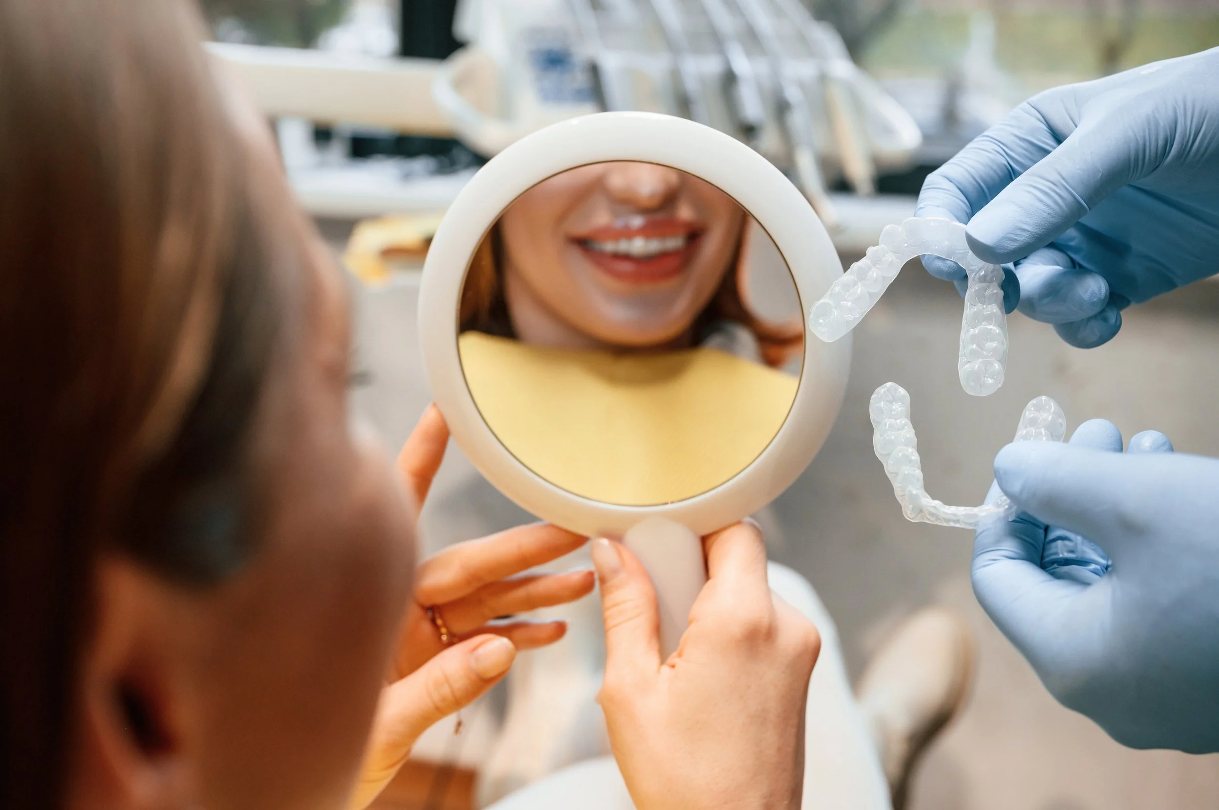 Dental professional fitting transparent clear aligner onto patient's teeth during orthodontic treatment appointment.