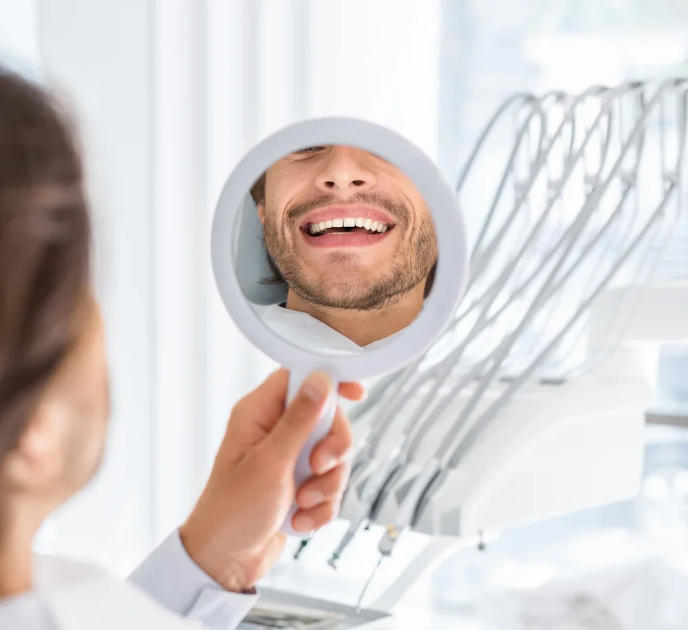 Happy male patient examining his new dental veneers in mirror during Boulder dentist appointment.