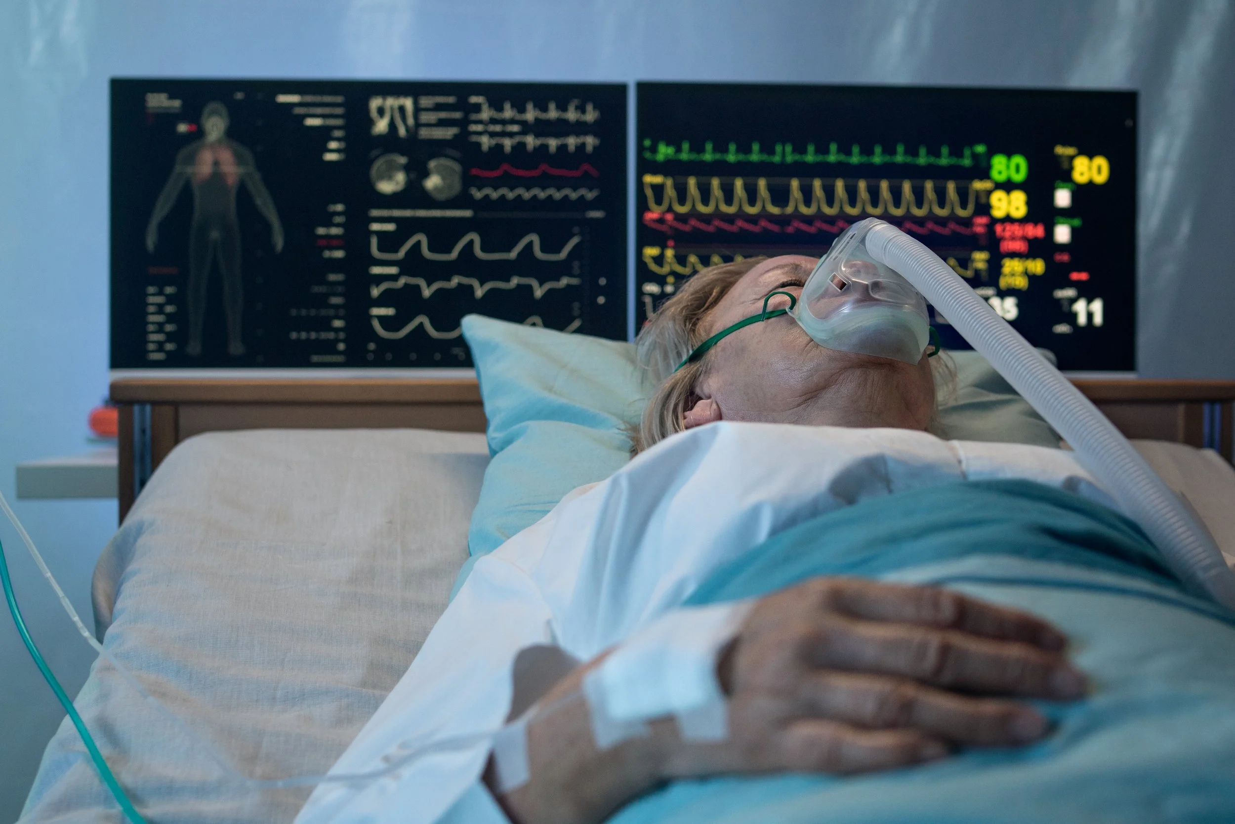 Patient rests in a sleep laboratory while connected to monitoring equipment and diagnostic screens.
