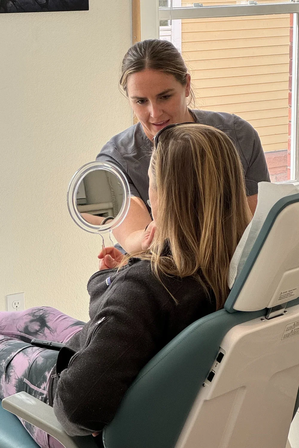 Dentist consulting with patient using mirror to discuss veneer options in Boulder dental office.