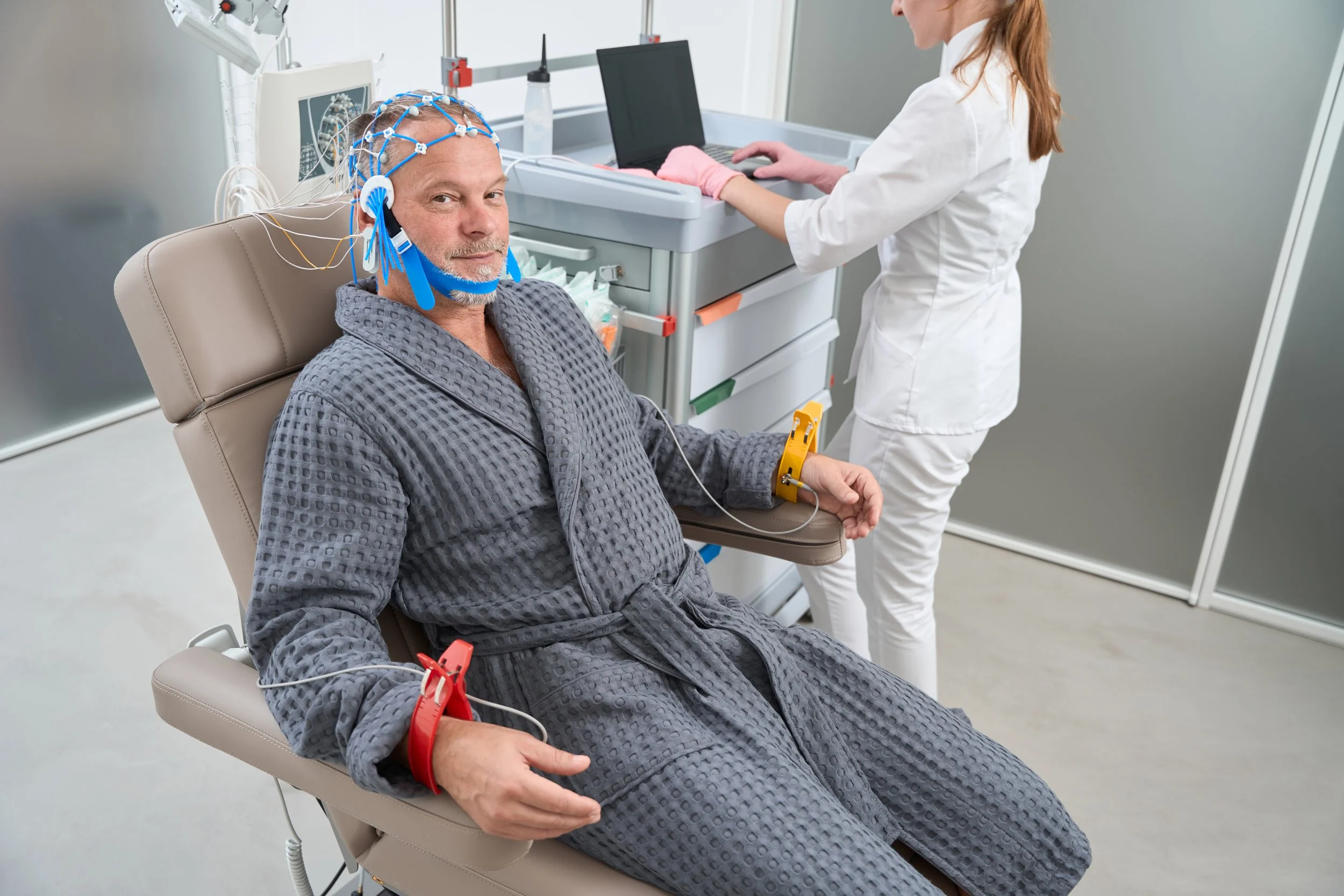 Man undergoes a monitored sleep study with facial sensors while a clinician records breathing data.