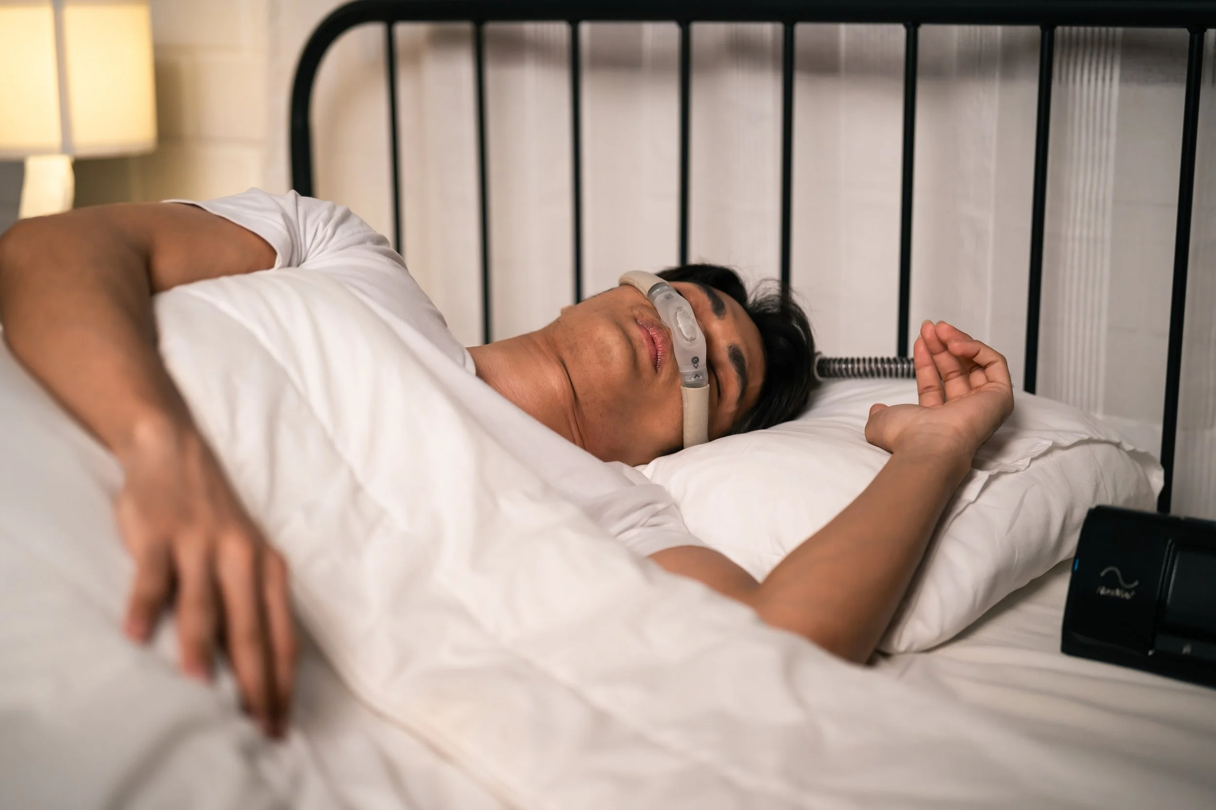 Man sleeping in bed while wearing a CPAP mask, illustrating sleep apnea treatment and nighttime breathing support.