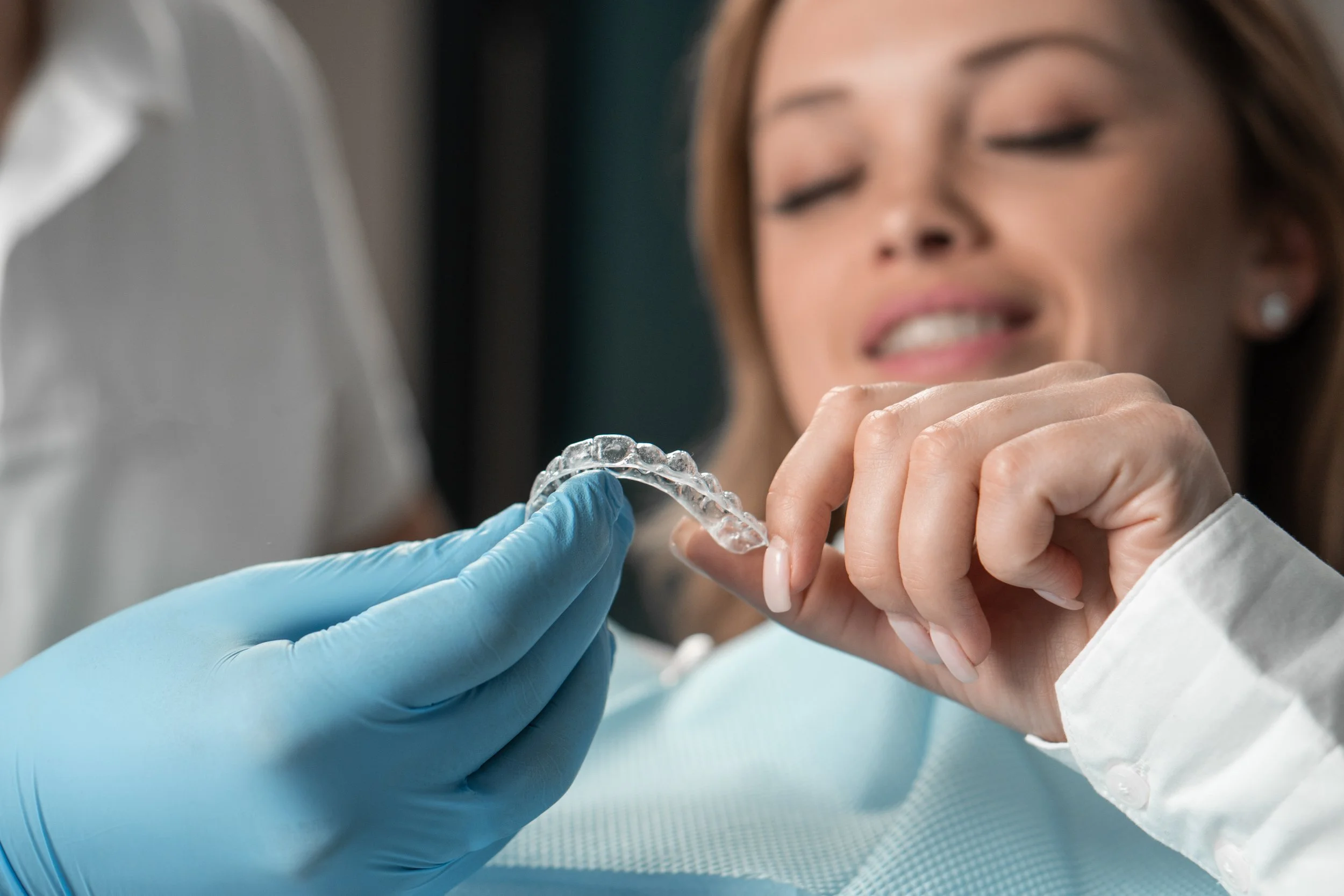 Dentist showing patient her smile progress using handheld mirror during clear aligner treatment checkup.