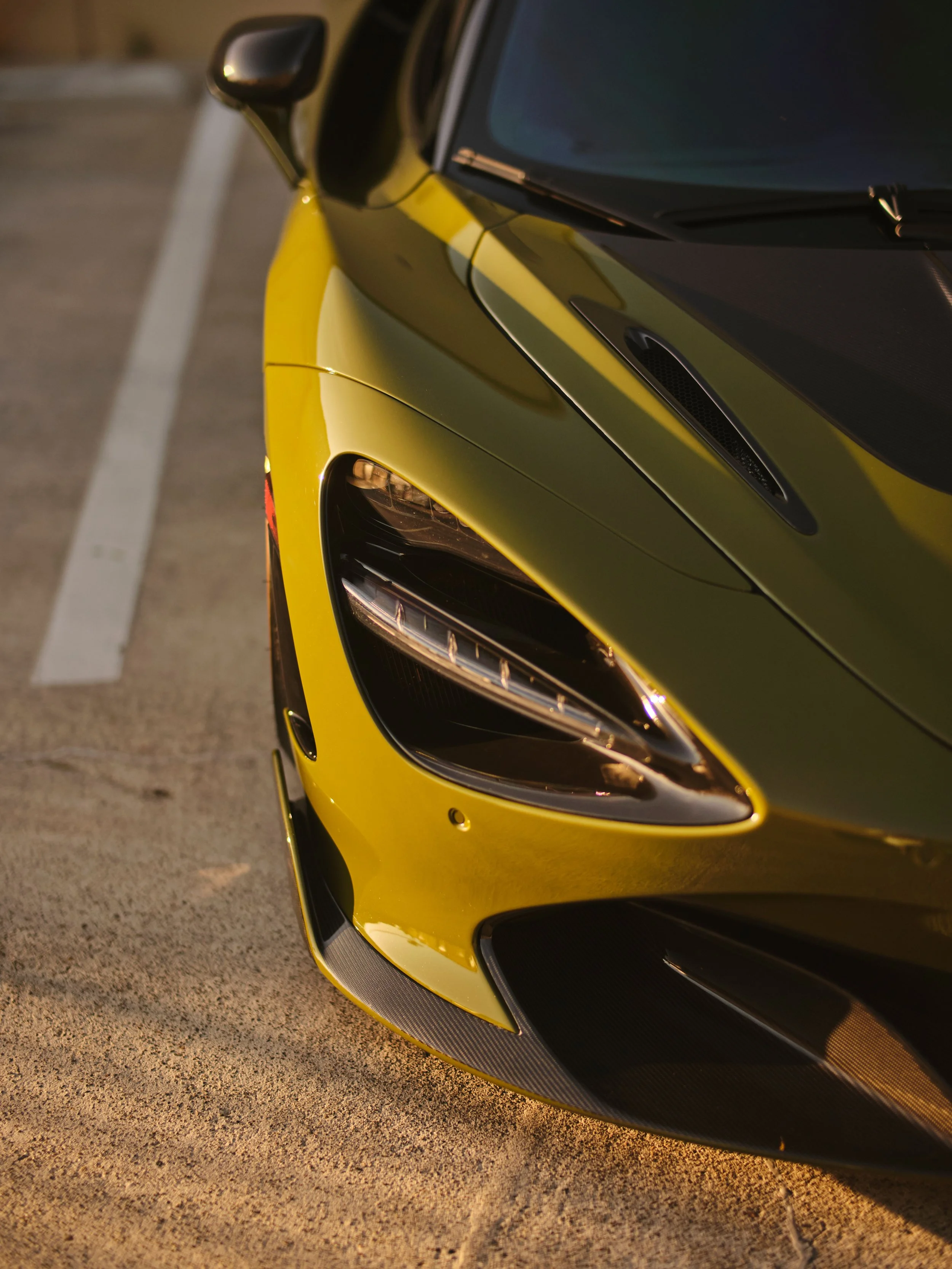 Close-up of the front corner of a yellow sports car parked on a concrete surface.