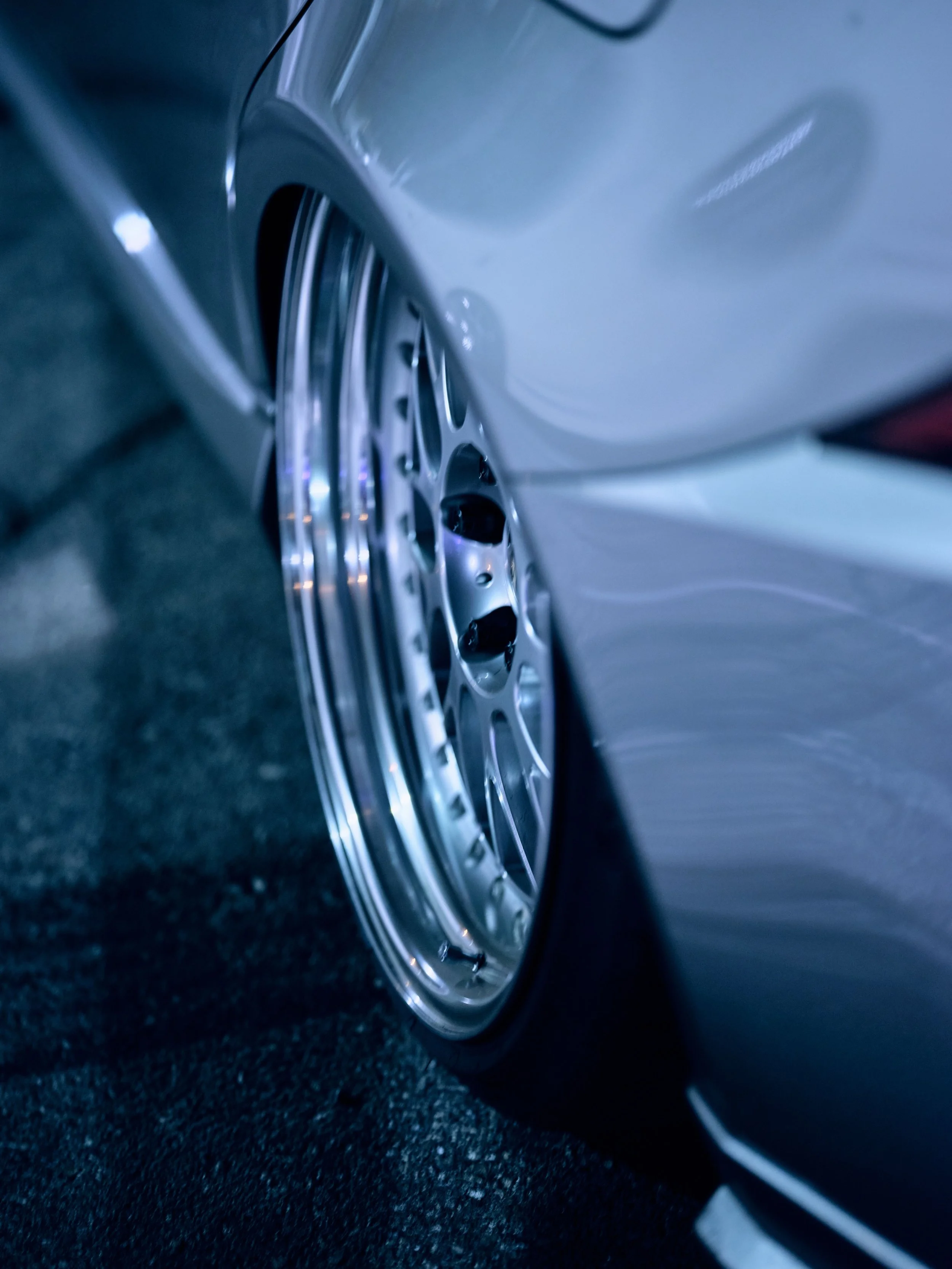 Close-up of a silver car's wheel with low-profile tire, parked on asphalt at night.