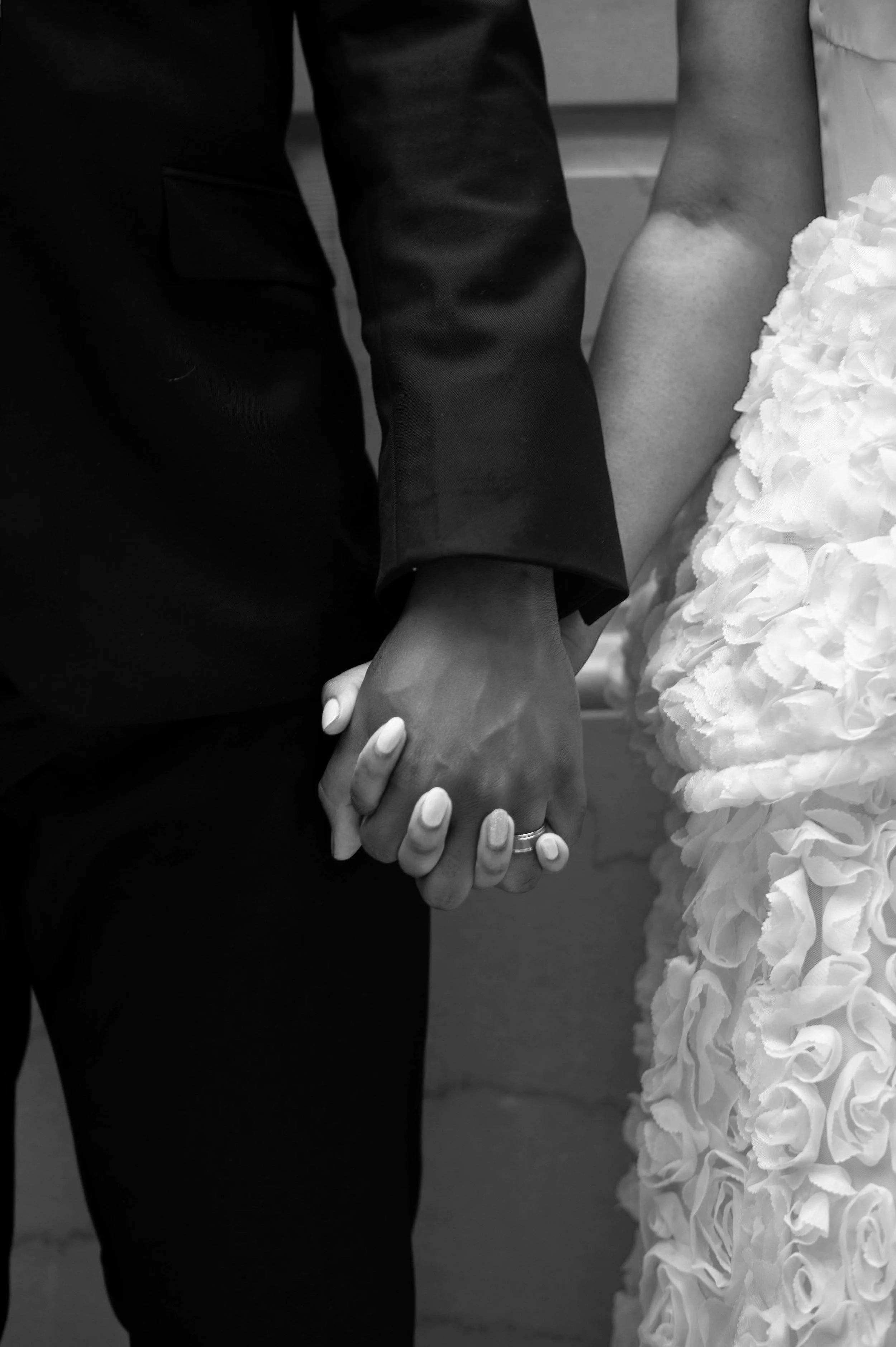 Close-up of a man and woman holding hands, with the woman in a wedding dress and the man in a suit.