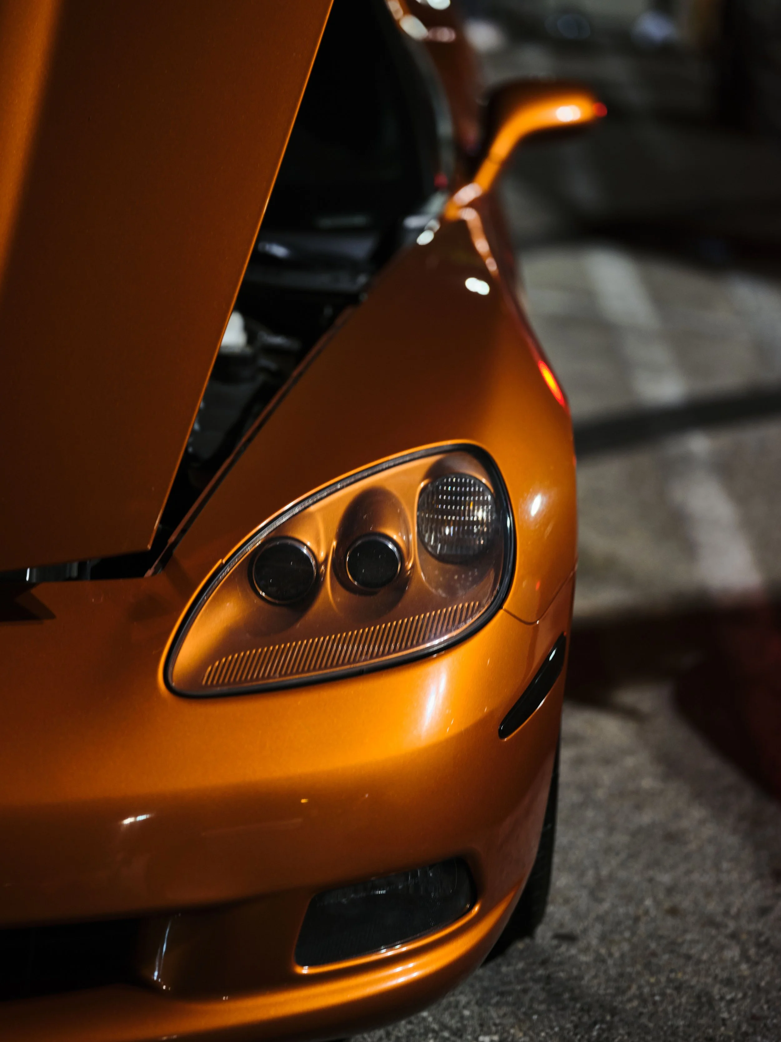 Close-up of the front left side of an orange sports car, showing the headlight and part of the hood.