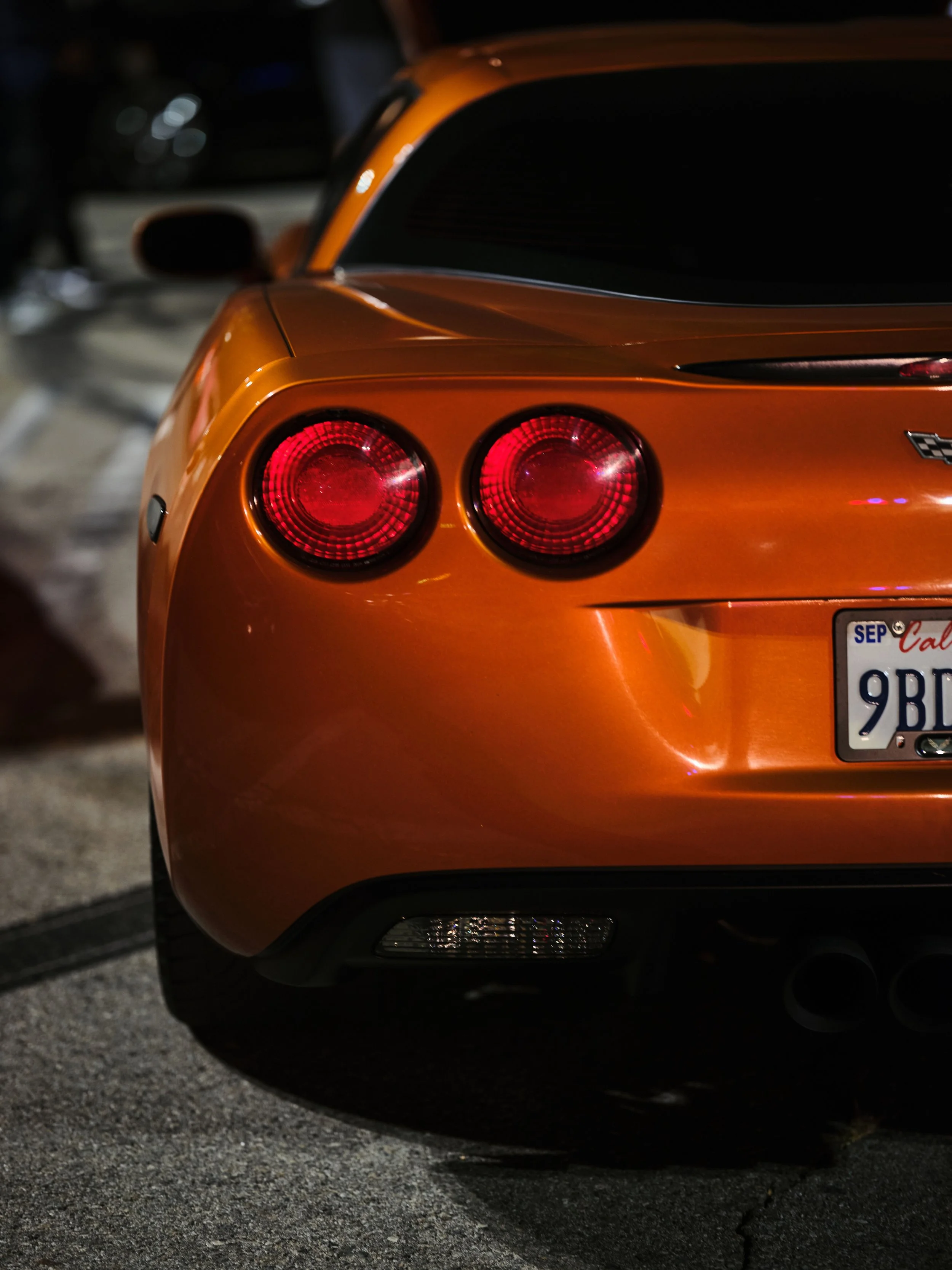 Close-up of the back of an orange sports car with round tail lights and a California license plate.