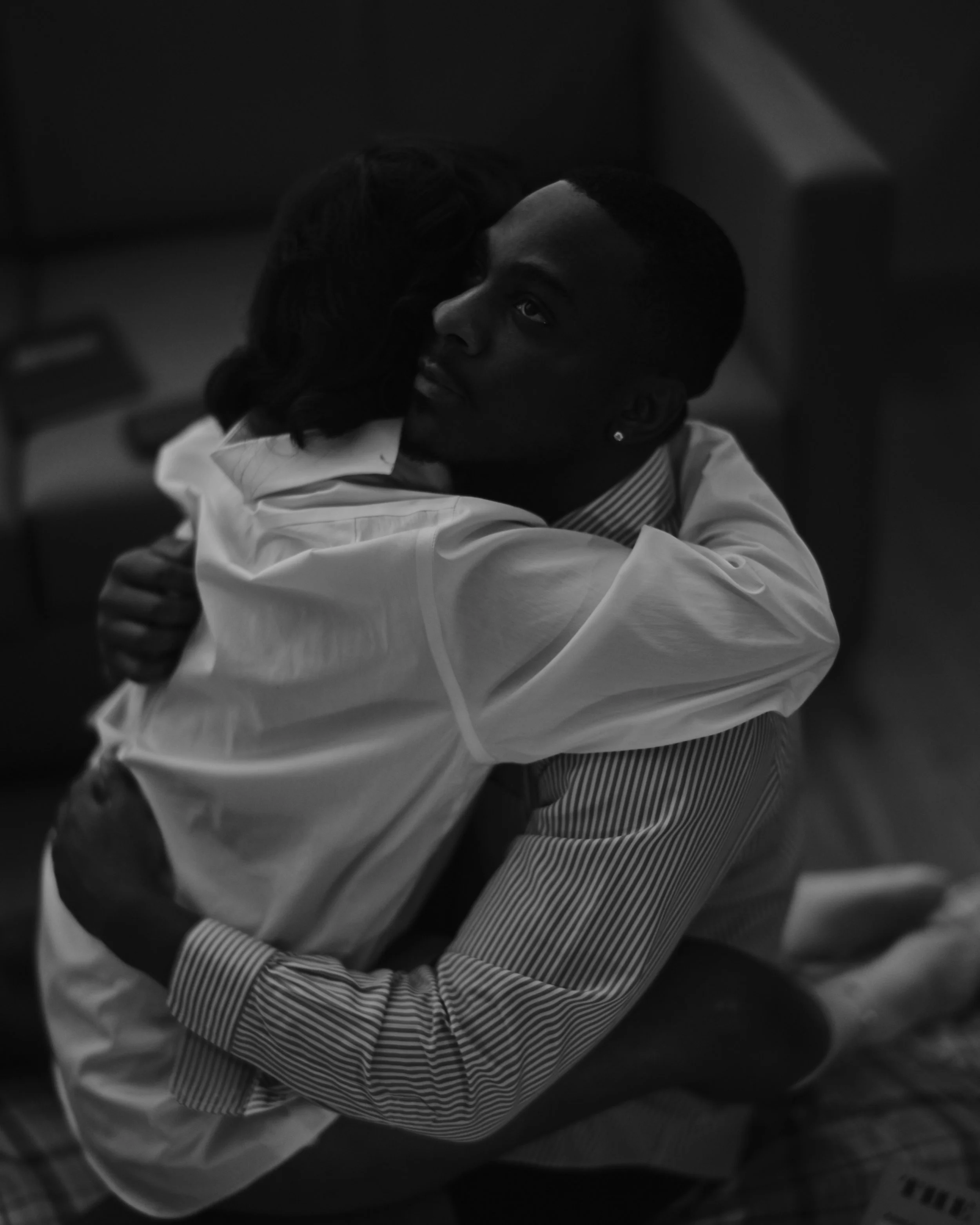 A man and woman hugging intimately, the man looking serious and the woman with her face turned away, in a black and white photograph.