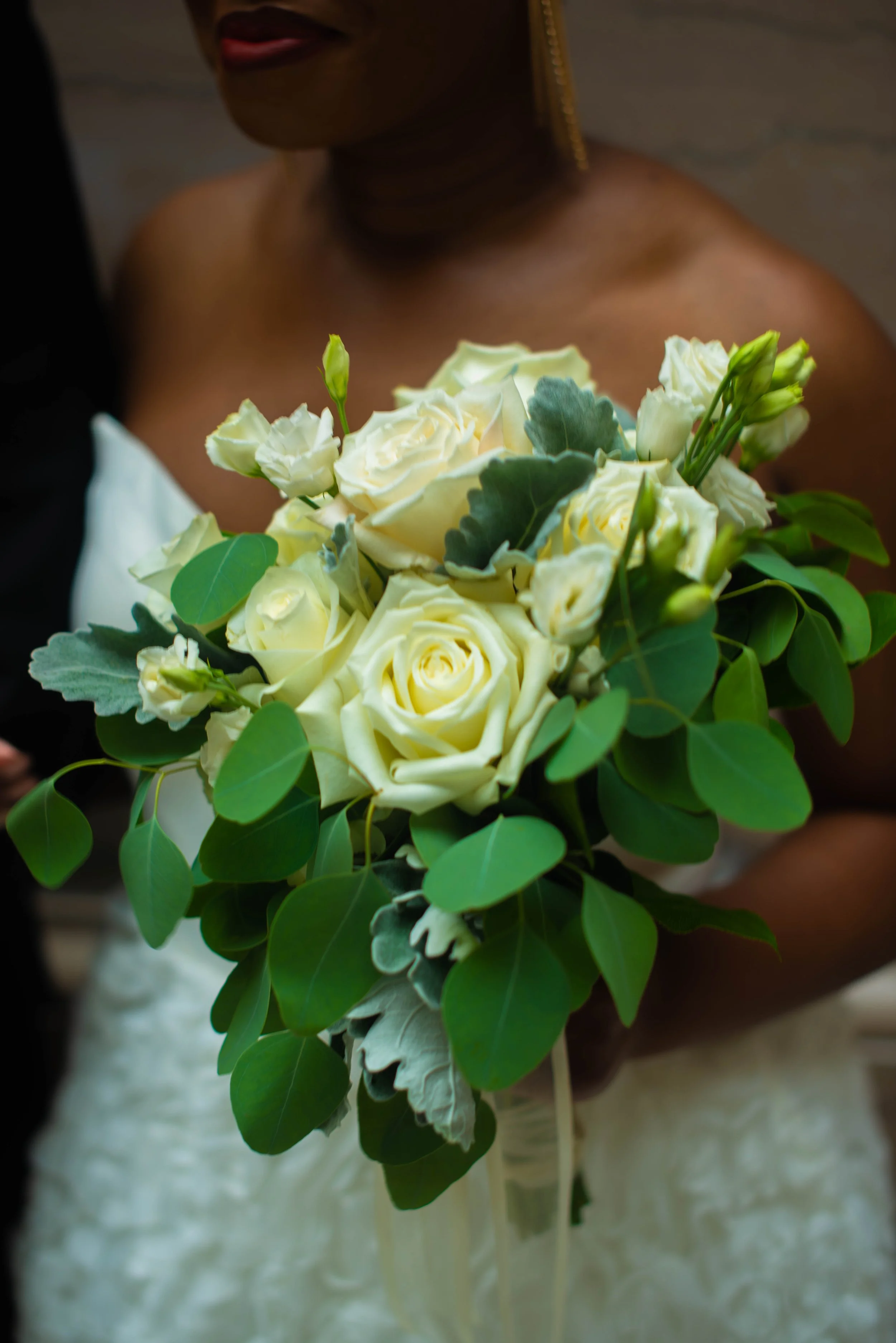 A woman in a white dress holding a bouquet of white roses, green leaves, and flower buds.