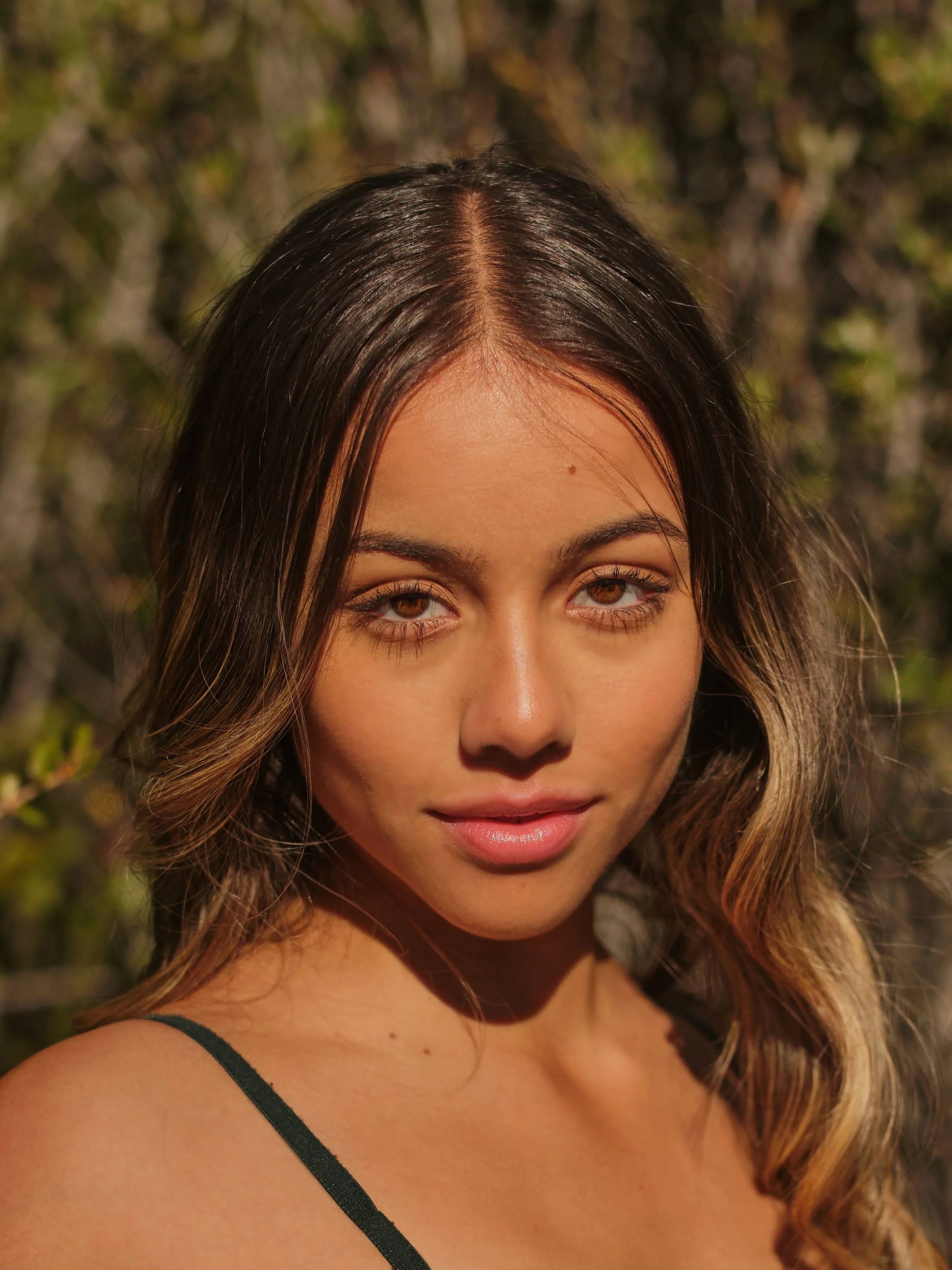 Close-up of a young woman with brown hair and brown eyes outdoors.