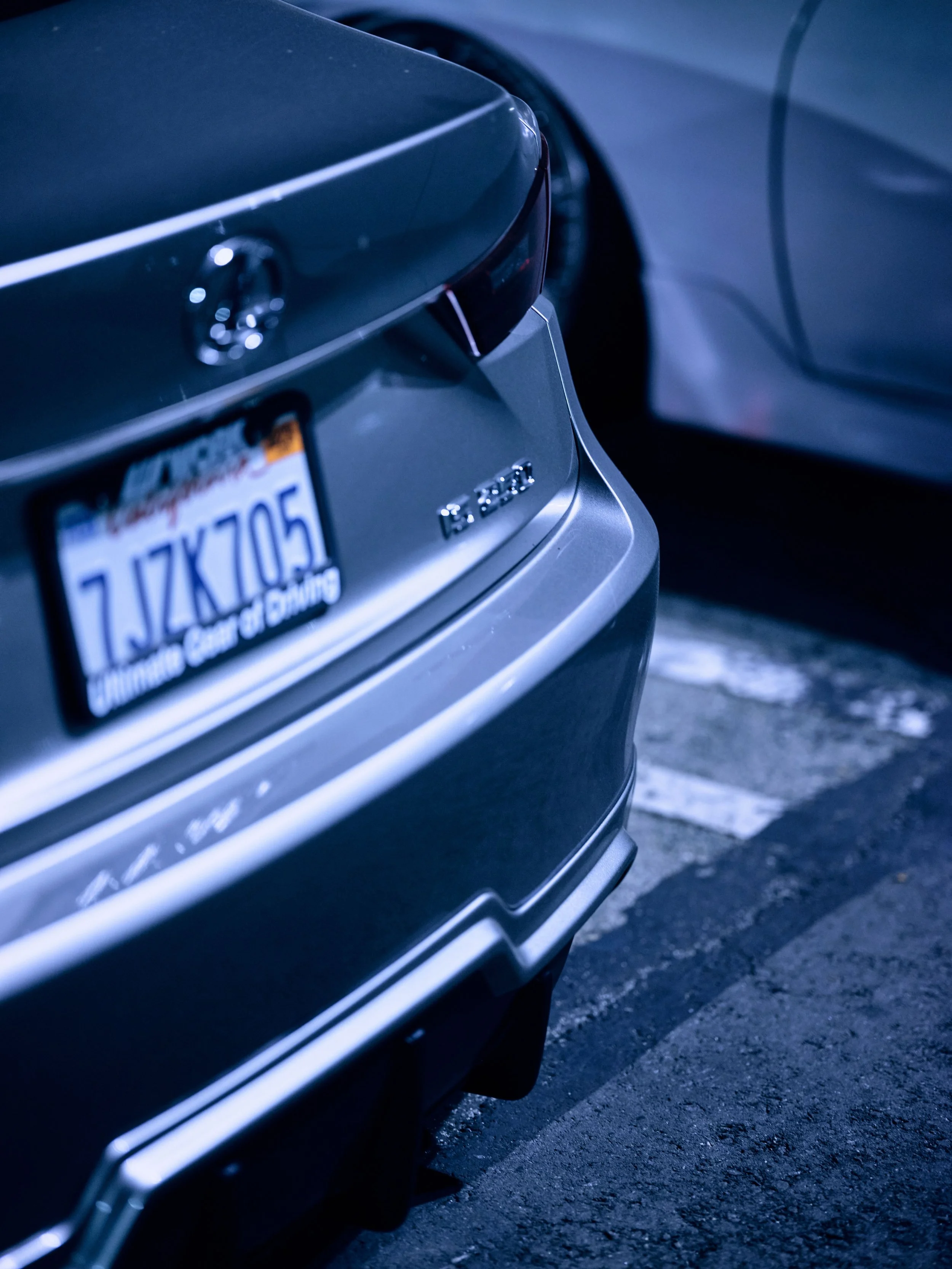 Close-up of the rear of a gray Cadillac vehicle parked in a parking lot, with the license plate and Cadillac badge visible.