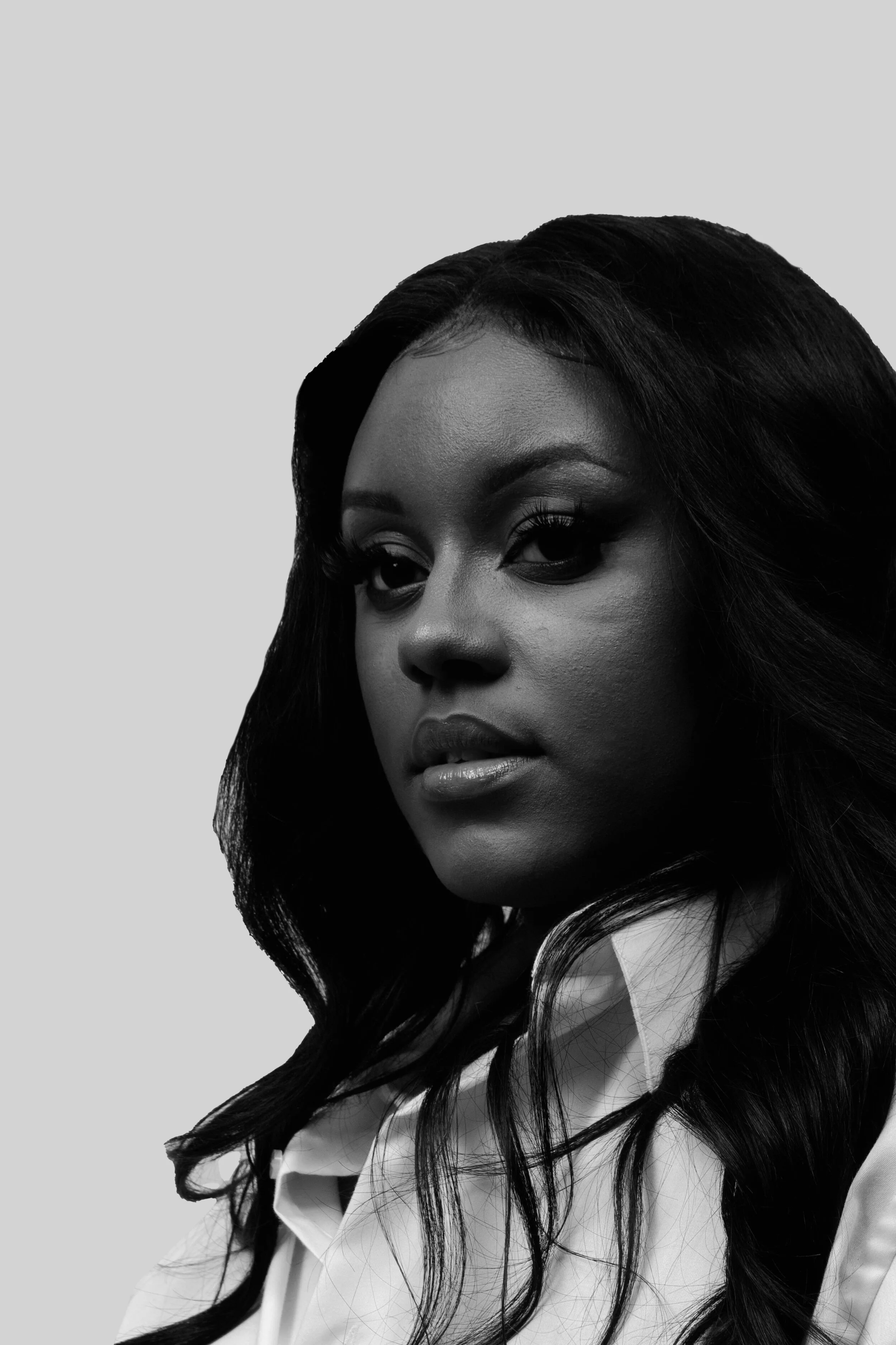 Close-up of a woman's face with long dark hair, wearing a white shirt, in black and white.