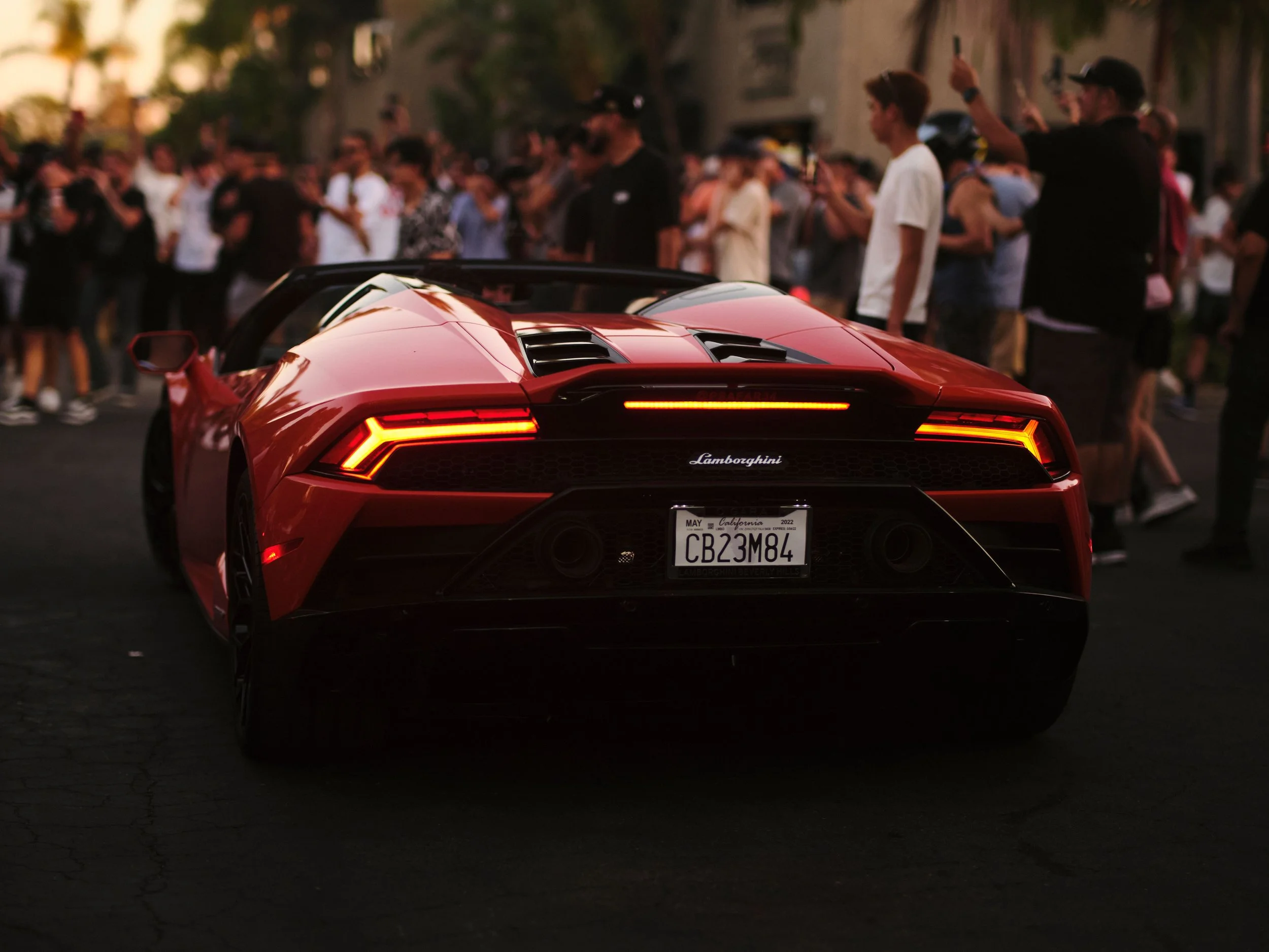 Red Lamborghini sports car viewed from the rear at an outdoor event with a crowd of people in the background.