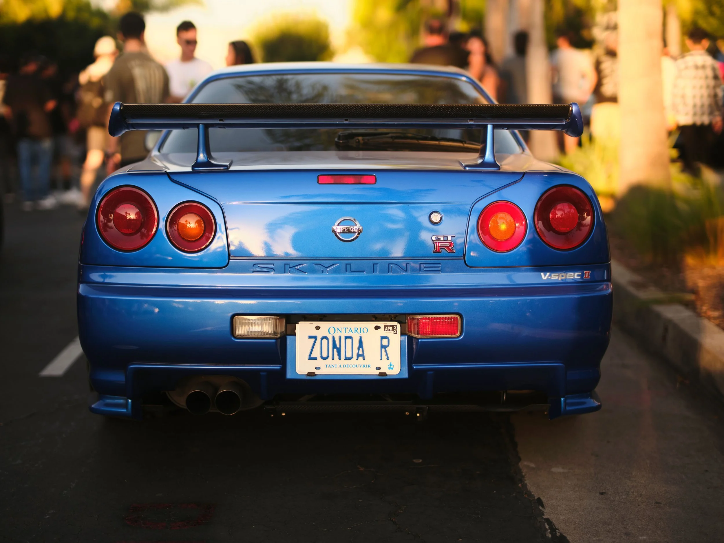 Blue Nissan Skyline GT-R V-Spec II car parked on the street with people in the background.