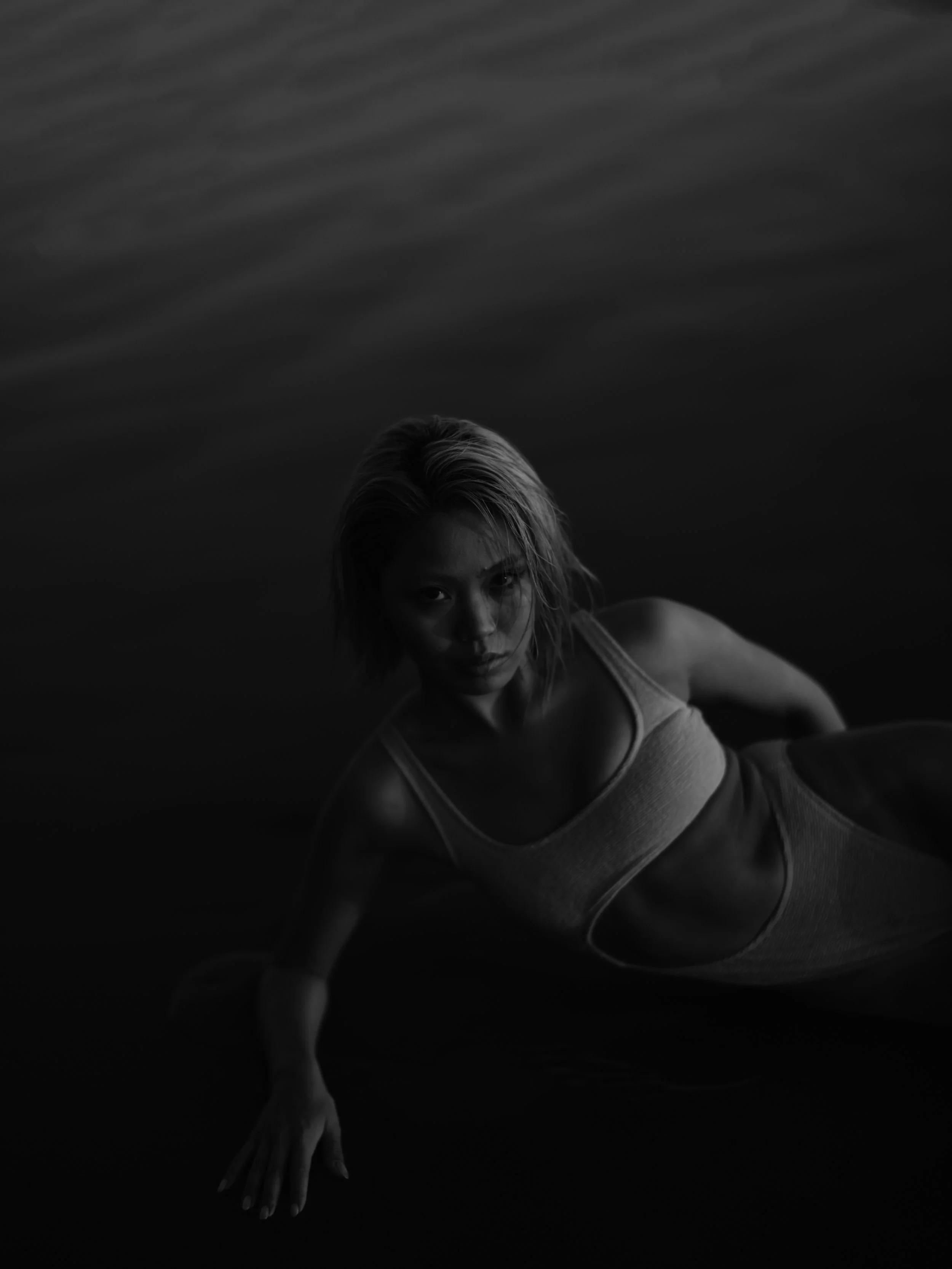 A woman with short blonde hair lying on her side in dark water, wearing a striped top, looking directly at the camera.