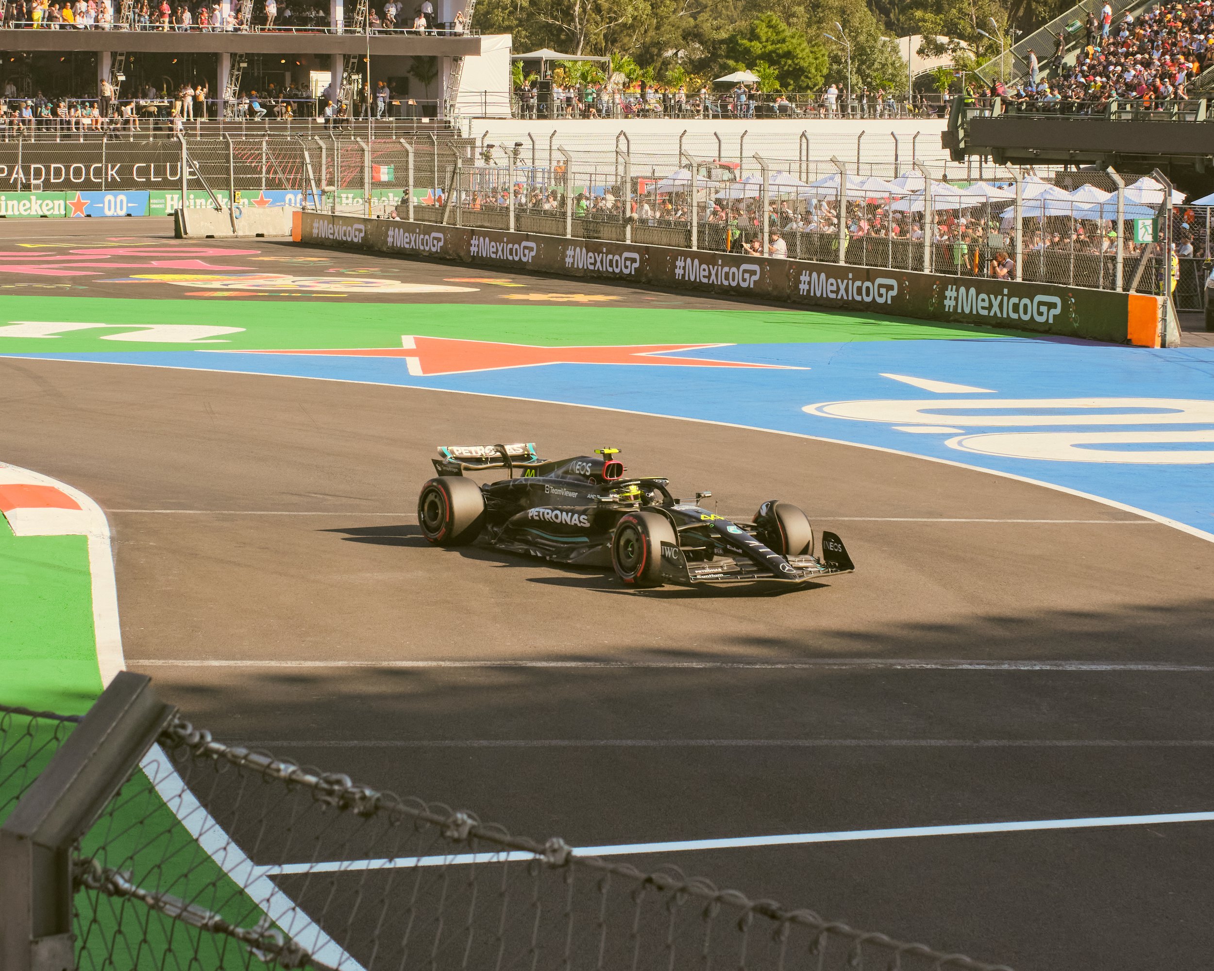 A Monaco Grand Prix race car on the track at the Mexico Grand Prix with spectators watching from the grandstands.