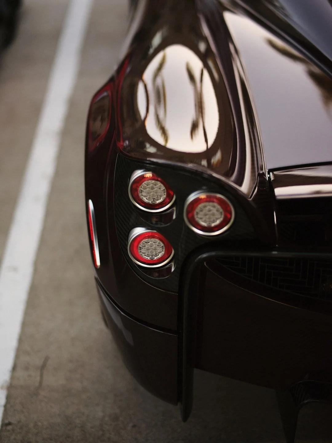 Close-up of the rear end of a black sports car, showing the taillights and part of the rear bumper, parked on a concrete surface.