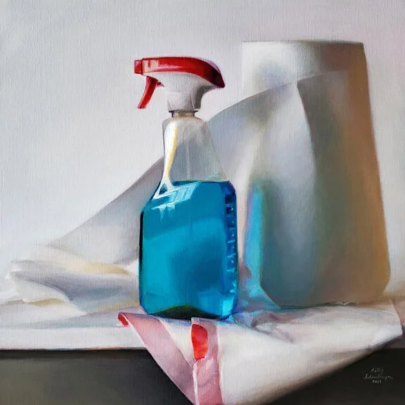 A spray bottle filled with blue cleaning solution and a partially visible white paper towel roll, sitting on a folded white plastic trash bag on a surface.