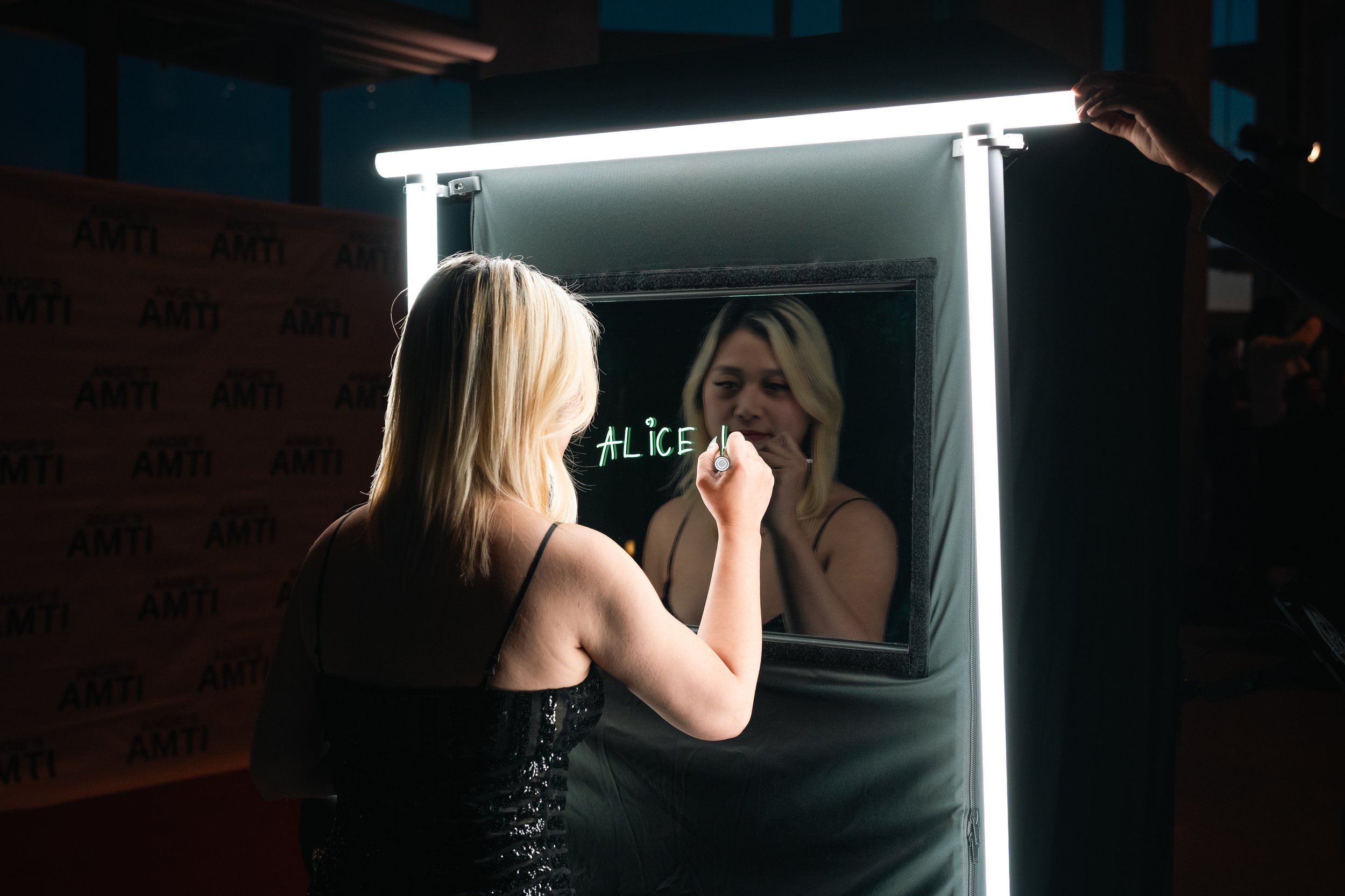 Guest writing her name on the scribble booth glass while the camera records through it, Toronto event