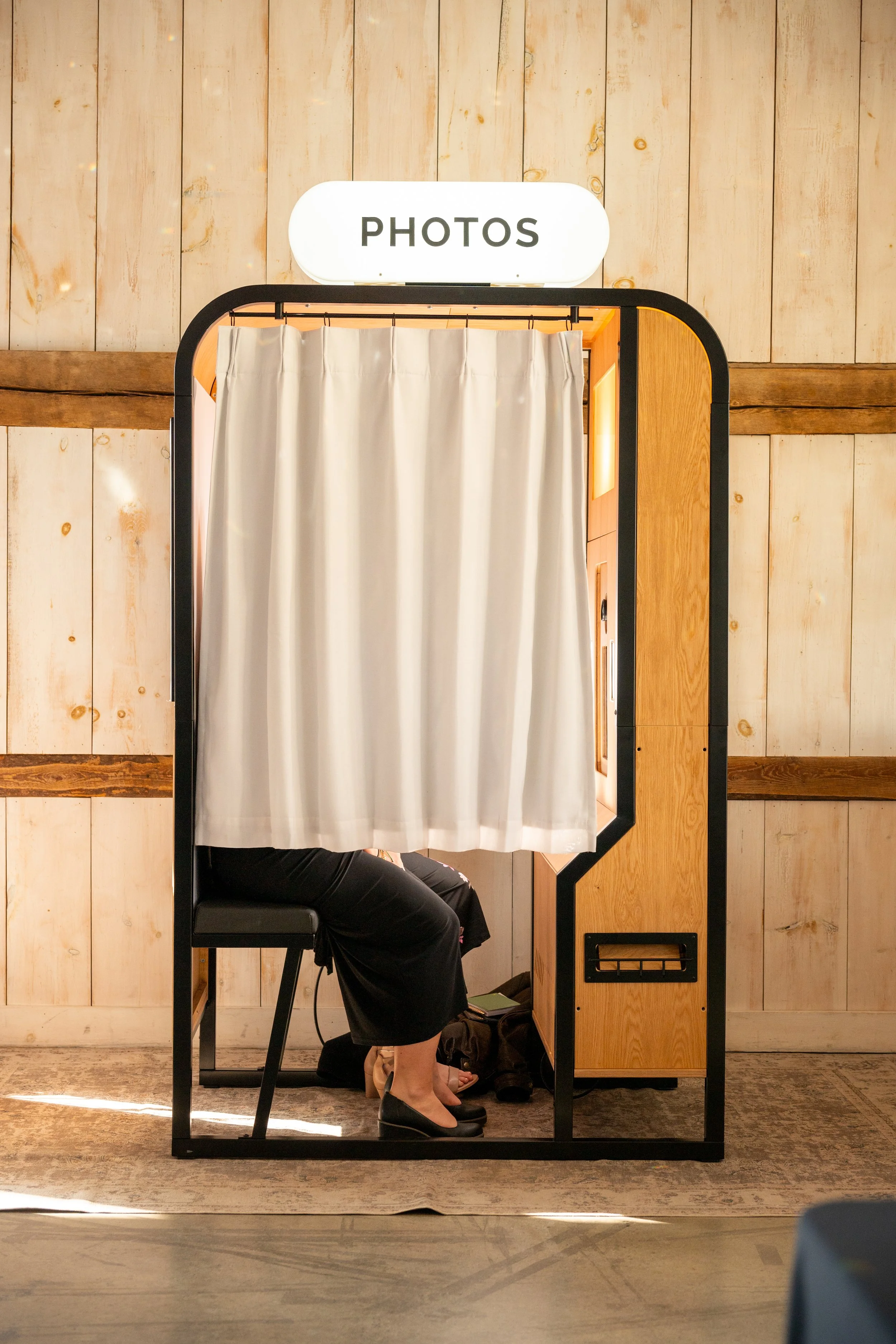 MDRN's enclosed midcentury vintage photo booth with a lit PHOTOS sign and privacy curtain drawn at a Stonefields Estate barn wedding near Ottawa