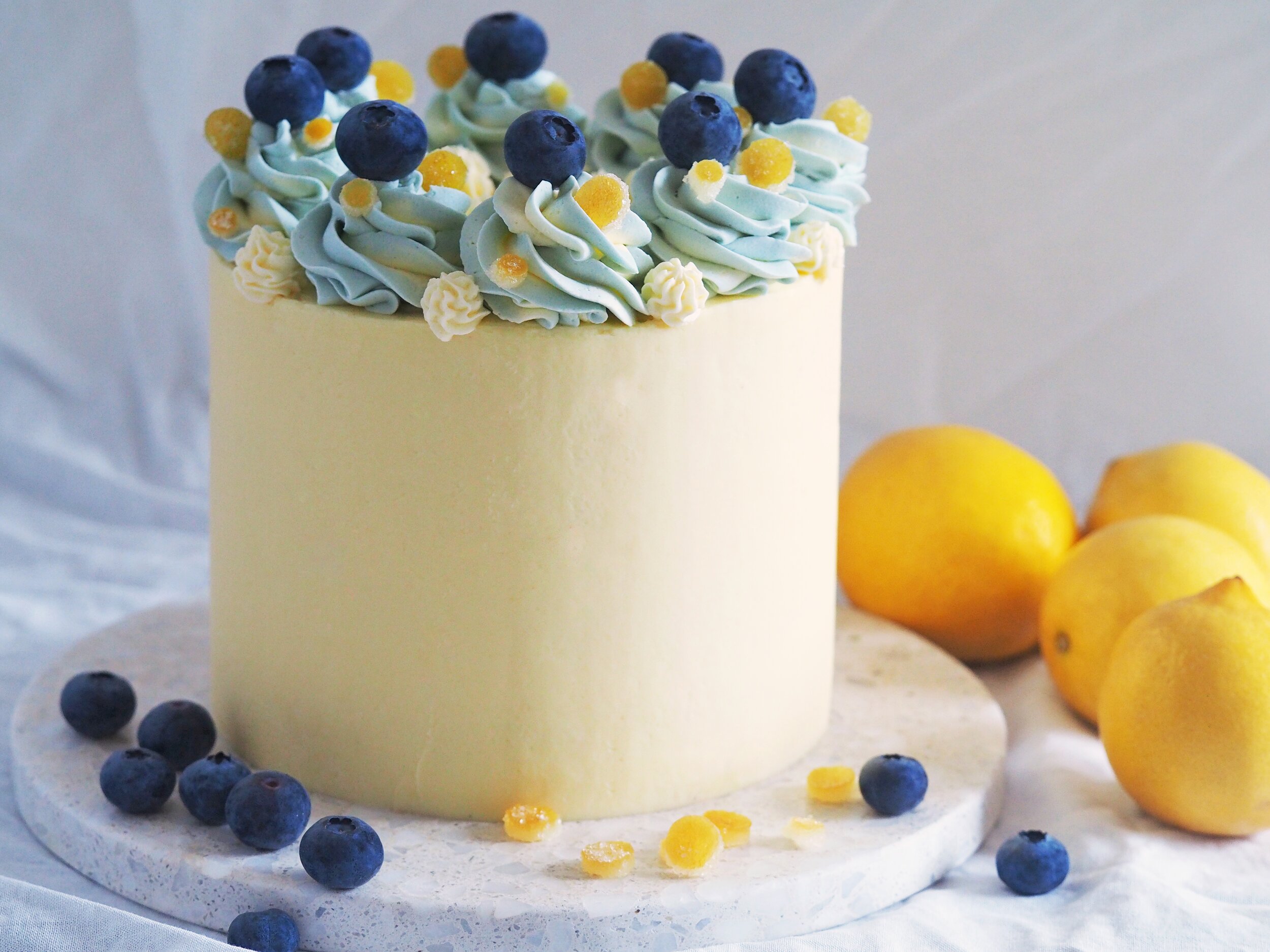 luscious lemon cake with vanilla butercream coating, decorated with blue vanilla buttercream swirls, hand-cut candied lemon confetti, and blueberries on top