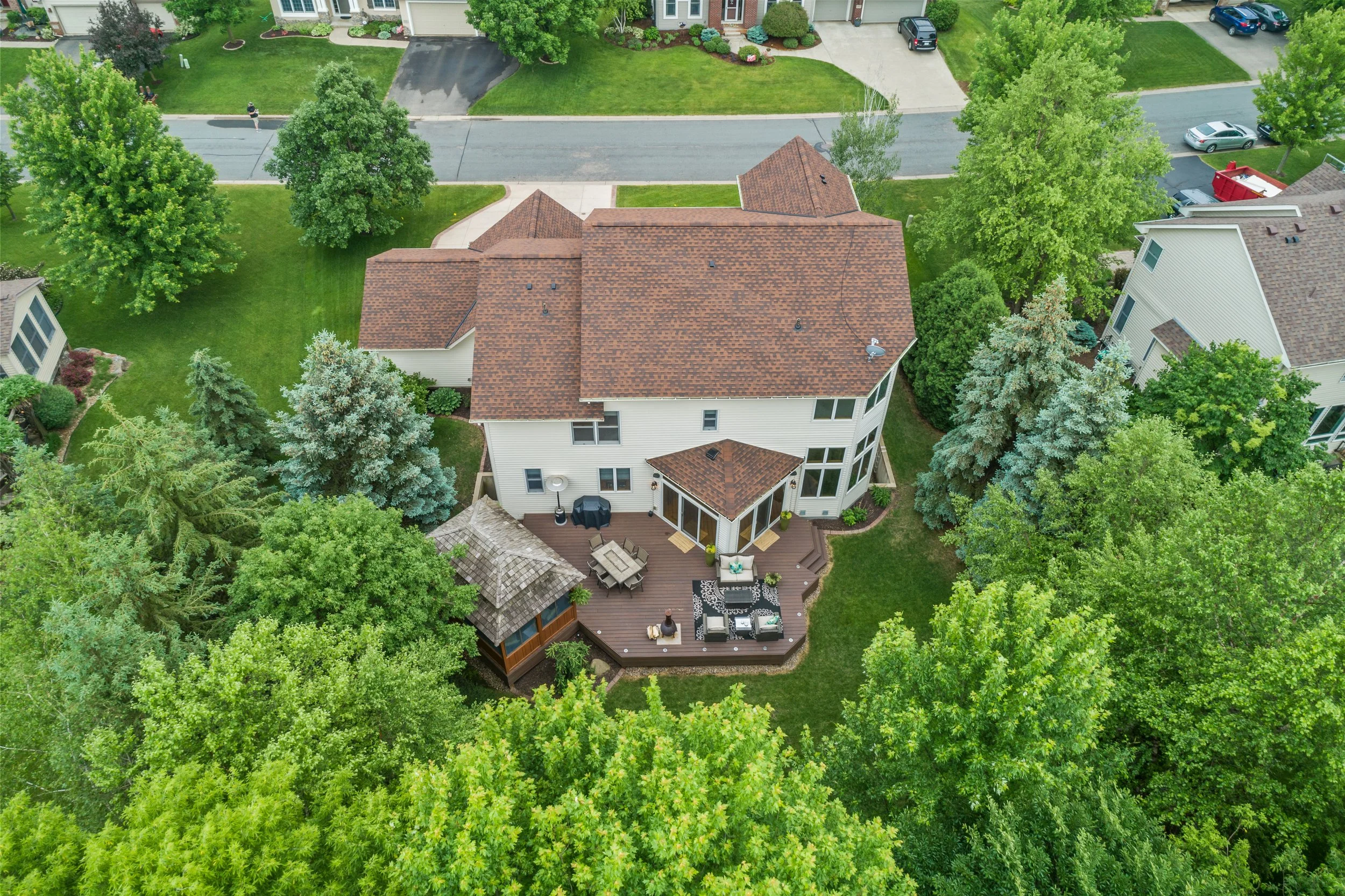 Aerial view of a suburban backyard equipped with a wooden deck, outdoor furniture, and lush green trees surrounding the area.