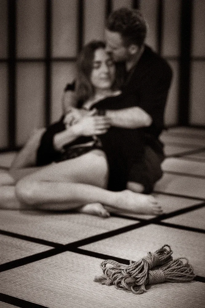 Couple in an intimate Tantric Shibari embrace on a tatami mat at Shibari Studio Berlin, with a coil of jute rope in the foreground.