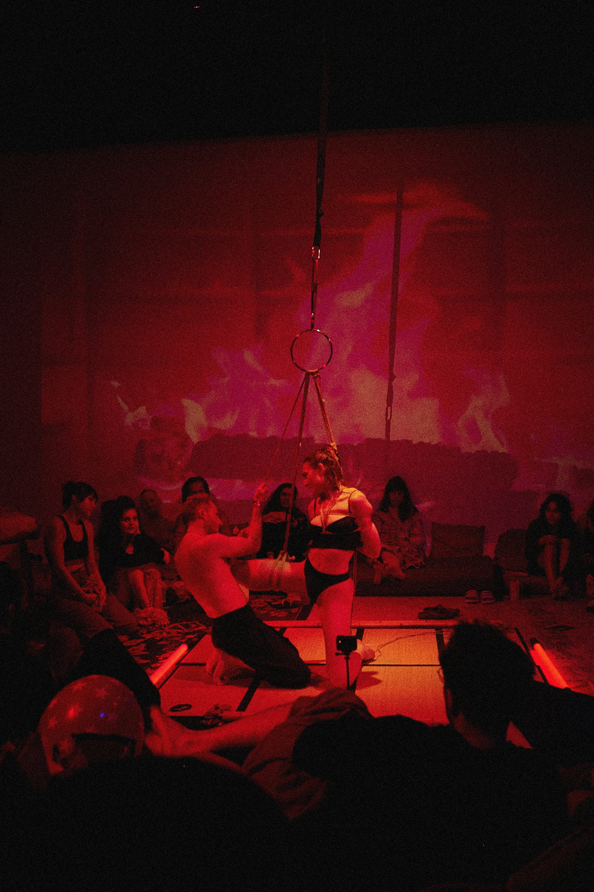 Dan Carabas and Dorcara performing a contemporary Shibari rope art piece in a large festival space with a live audience surrounding them.