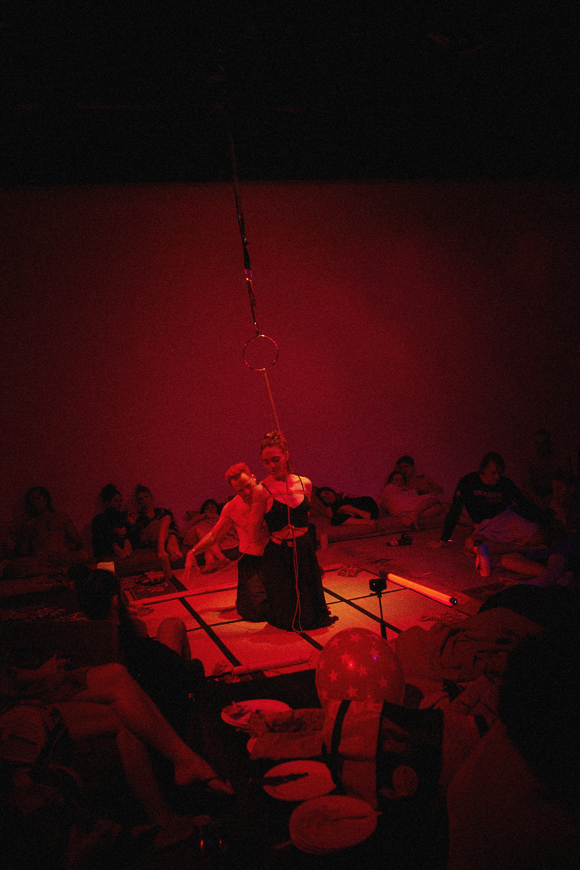 Dan Carabas and Dorcara performing a contemporary Shibari rope art piece in a large festival space with a live audience surrounding them.