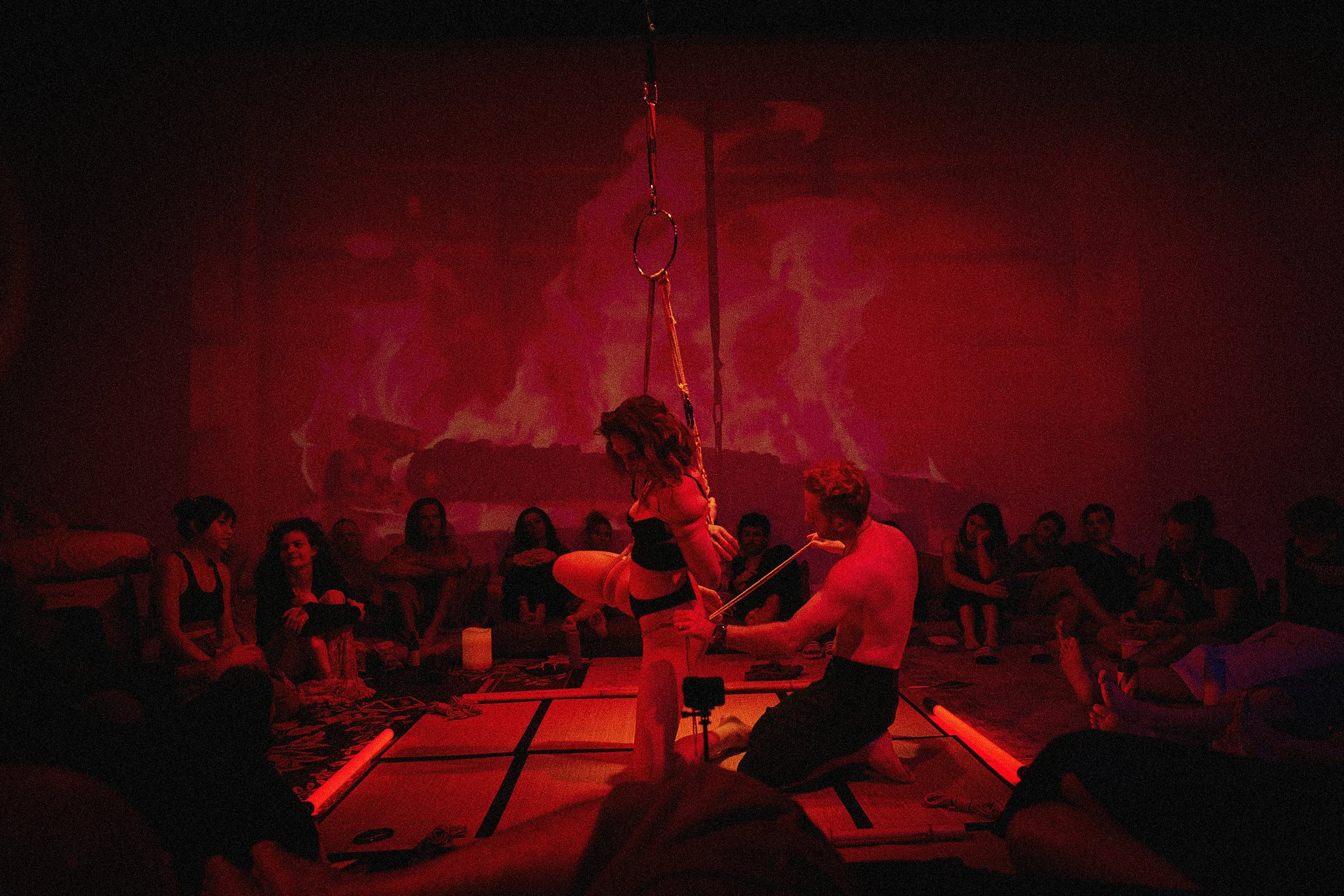 Immersive Shibari rope art performance by Dan Carabas and Dorcara in a festival space with atmospheric lighting and sculptural body composition.