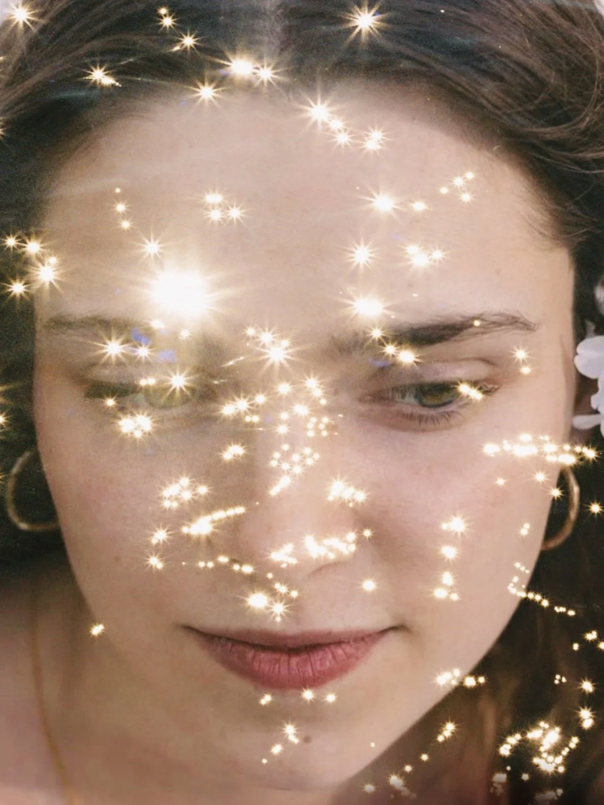 Close -up of a woman's face, expression is gentle and serene. Overlayed as a double exposure are sparkles from sunlight on water.