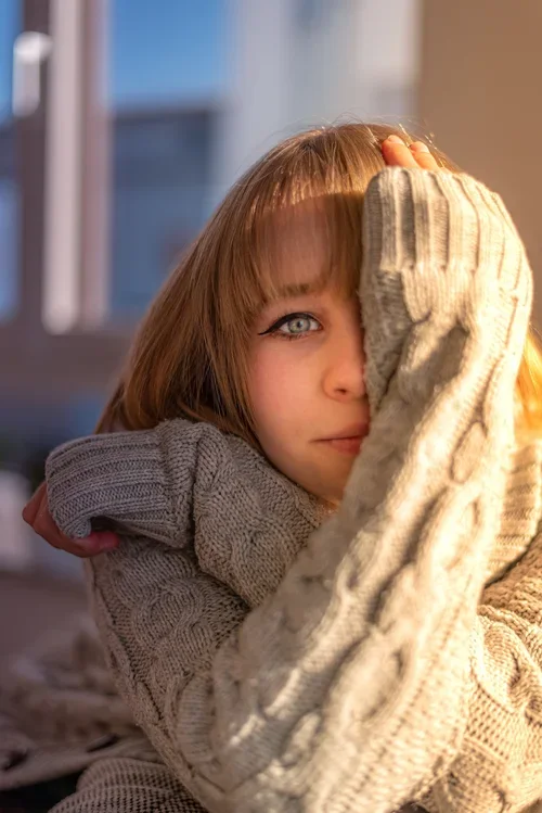Woman in a chunky knit jumper with her sleeve over half her face, looking at the camera, for adult ADHD therapy in Perth