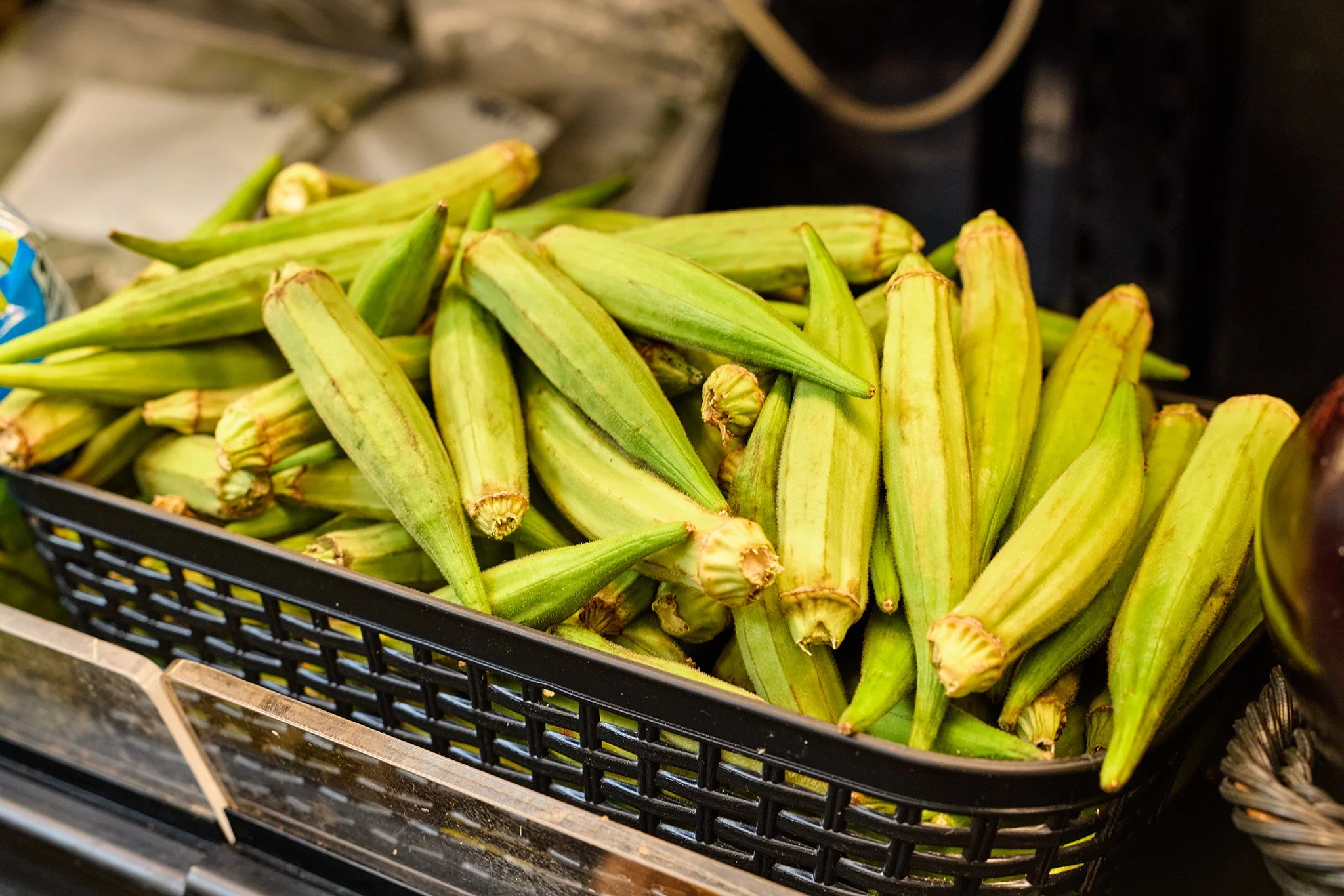 Fresh okra in a black plastic basket at a market