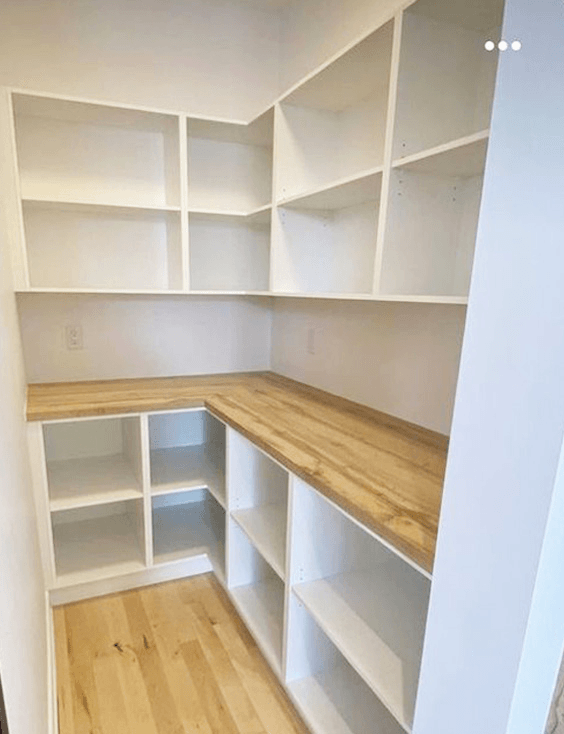 Empty white built-in corner shelves and a wooden countertop in a room.