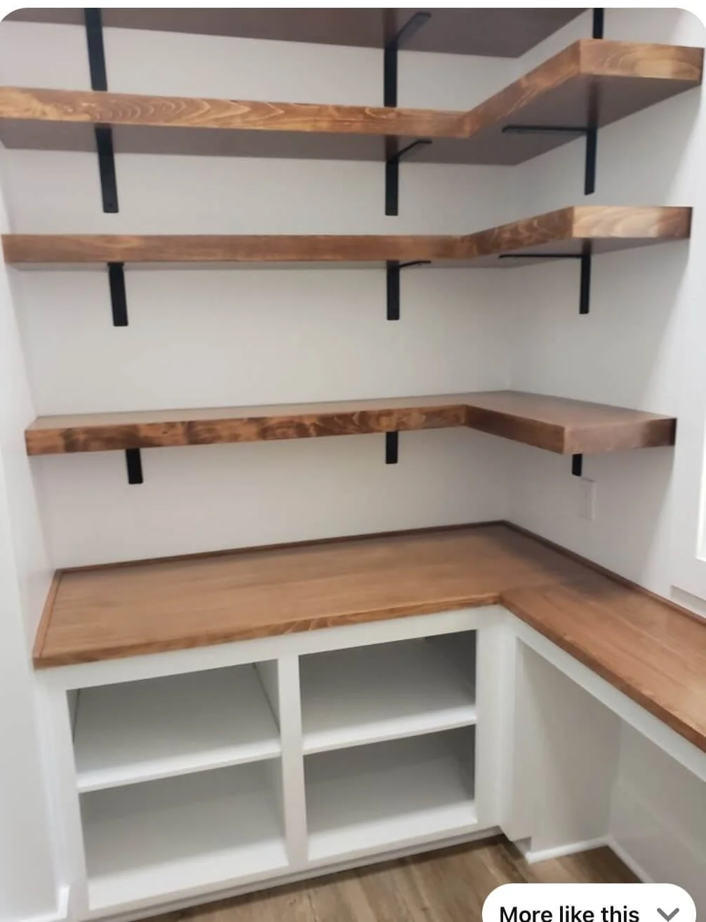 Empty built-in shelves and countertop in a small room or pantry, with three wooden floating shelves on black brackets on the wall, and white open cubbies at the bottom.