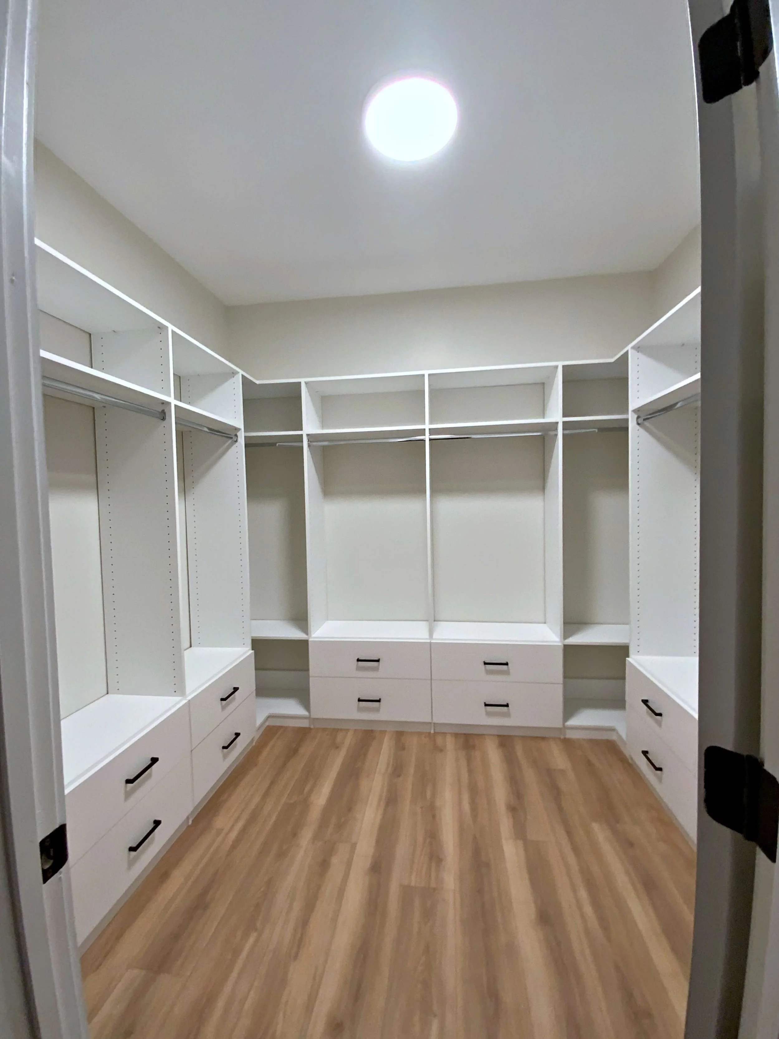 Empty walk-in closet with white shelving and drawers, hardwood floor, and a ceiling light.