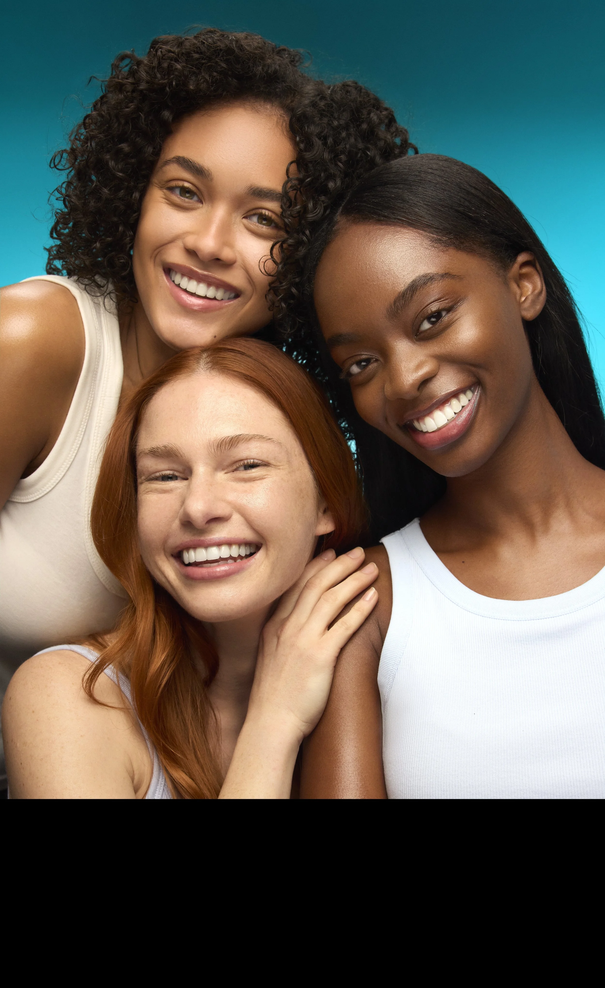 Four women of diverse ethnicities smiling and close together for a group selfie. Background is a gradient blue.