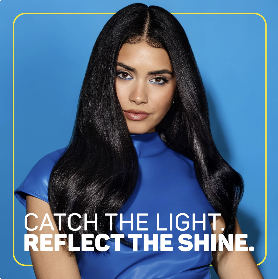 A woman with long, straight black hair and makeup, wearing a shiny blue top, against a blue background with yellow border, with the text 'Catch the Light. Reflect the Shine.'