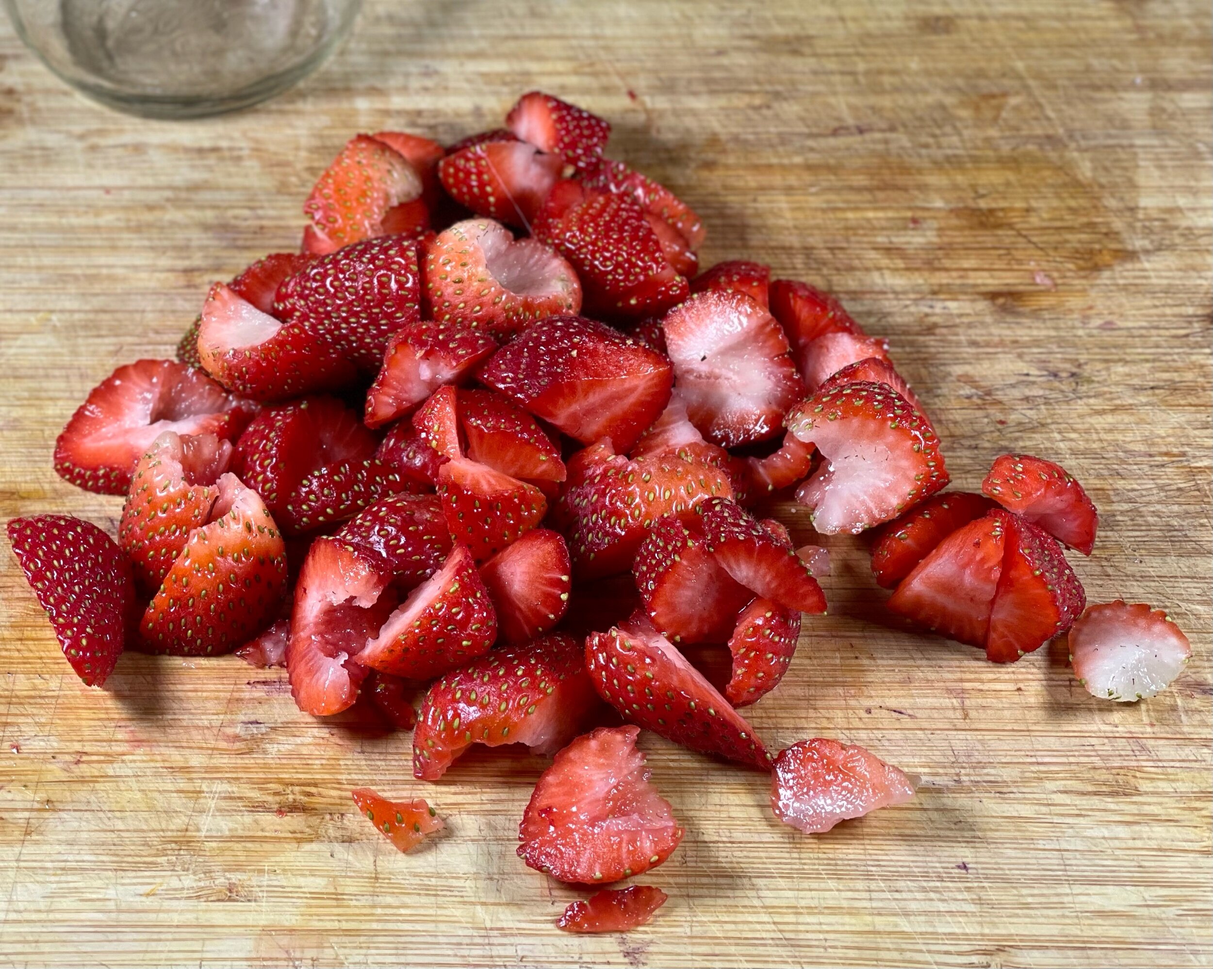  Pile of strawberries rough chopped onto of a wooden cutting board. 