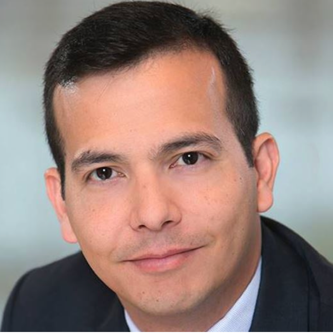 Close-up of a man in a suit with short dark hair and a slight smile in a professional setting.
