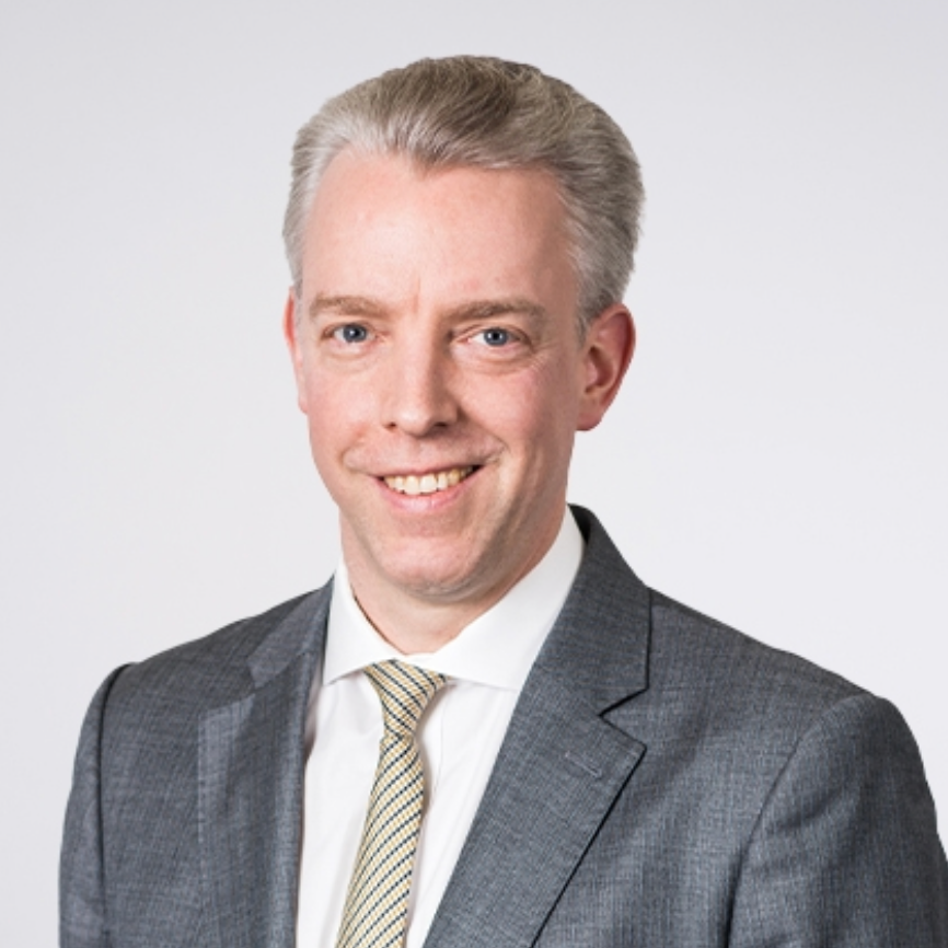portrait of a man in a gray suit, white shirt, and yellow tie smiling against a plain white background.